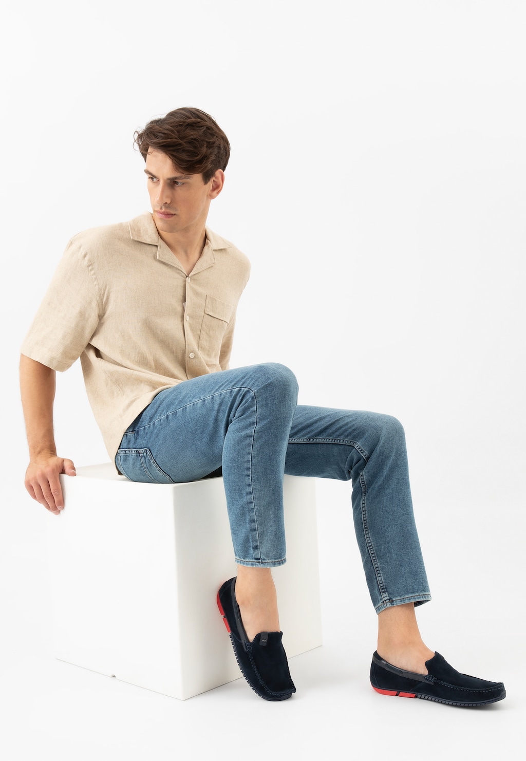 Granatowe mokasyny męskie Wojas 10190-76 z czerwonymi akcentami na podeszwie prezentowane na modelu w beżowej koszuli i jeansach, siedzącym na białym postumencie.