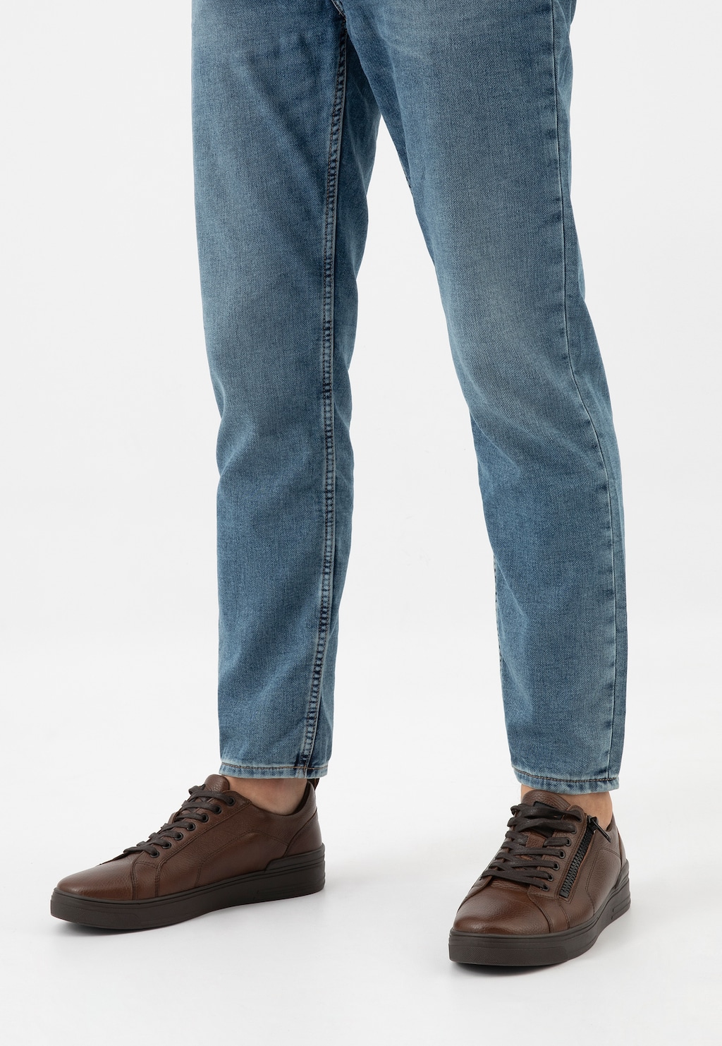 Ciemnobrązowe trampki męskie Wojas model 10149-52 z ozdobnym zamkiem, noszone do niebieskich jeansów, widok z perspektywy frontalnej na dół sylwetki.