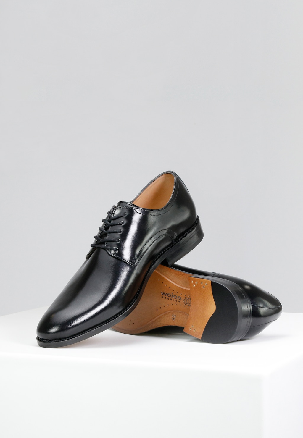 Eleganckie czarne półbuty męskie Wojas model 10055-51 z linii PREMIUM. Widok z góry na dwa błyszczące buty ze skórzaną podeszwą i charakterystycznym logo marki wewnątrz.