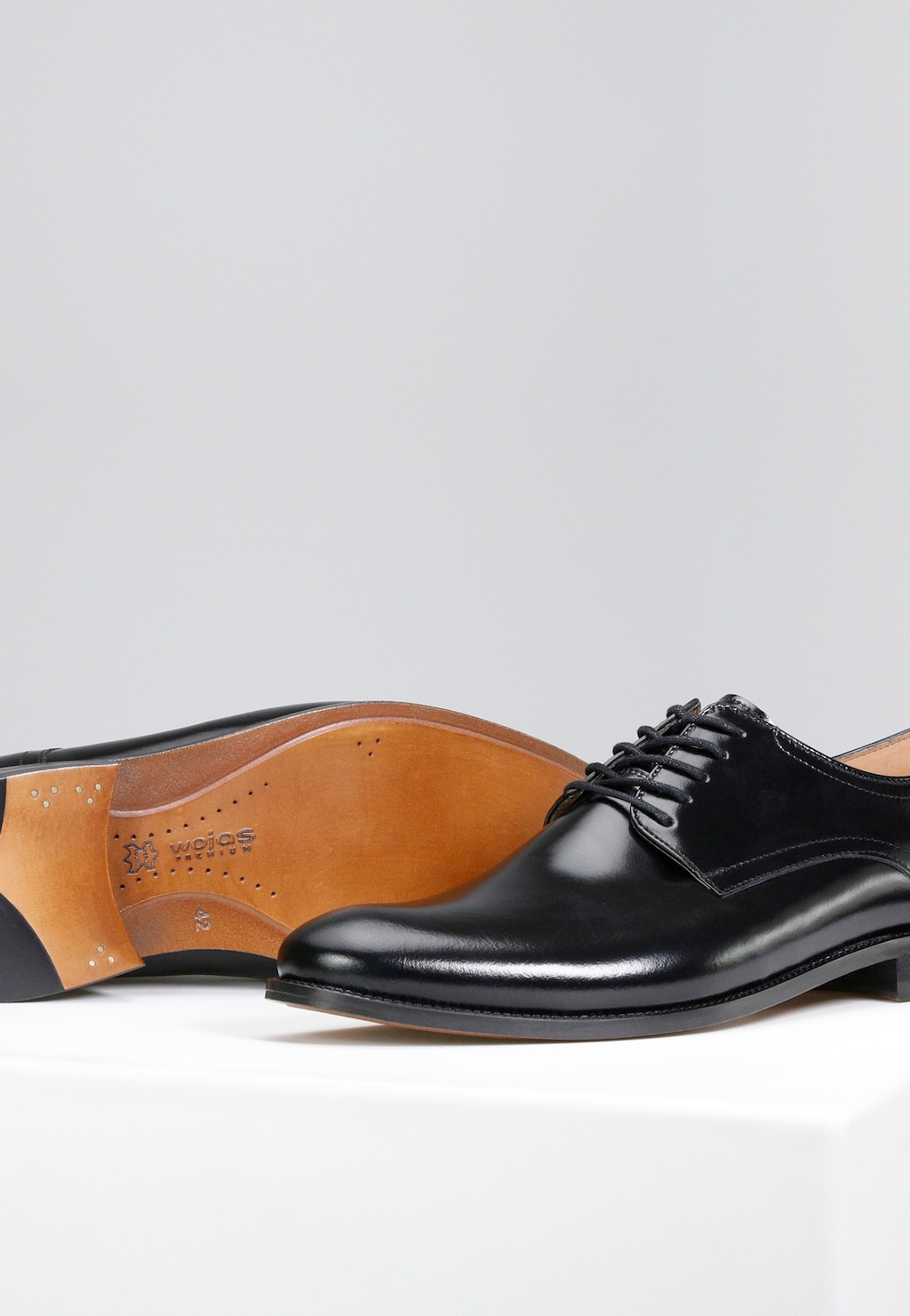 Eleganckie czarne półbuty męskie Wojas model 10055-51 z linii PREMIUM, widoczne z boku. Skórzane buty ze sznurowaniem i brązową podeszwą z widocznym logo marki.