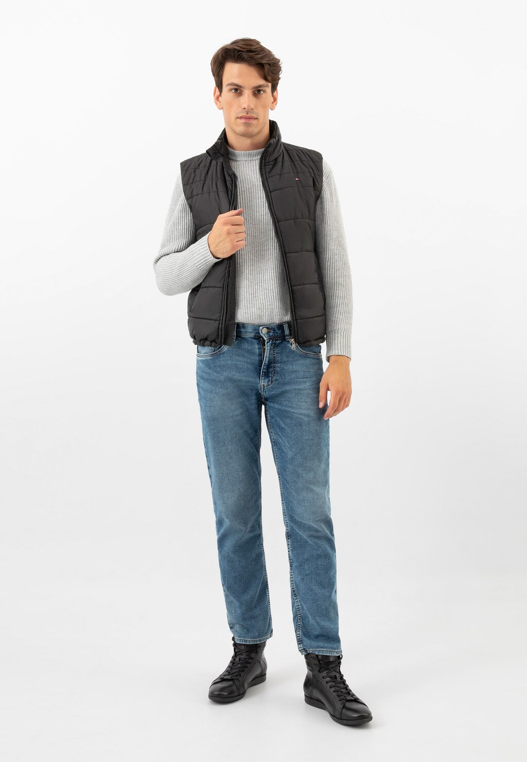 Model w czarnej kamizelce, szarym swetrze i jeansach prezentuje trzewiki męskie Wojas model 24093-51 - czarne skórzane sneakersy w casualowej stylizacji.