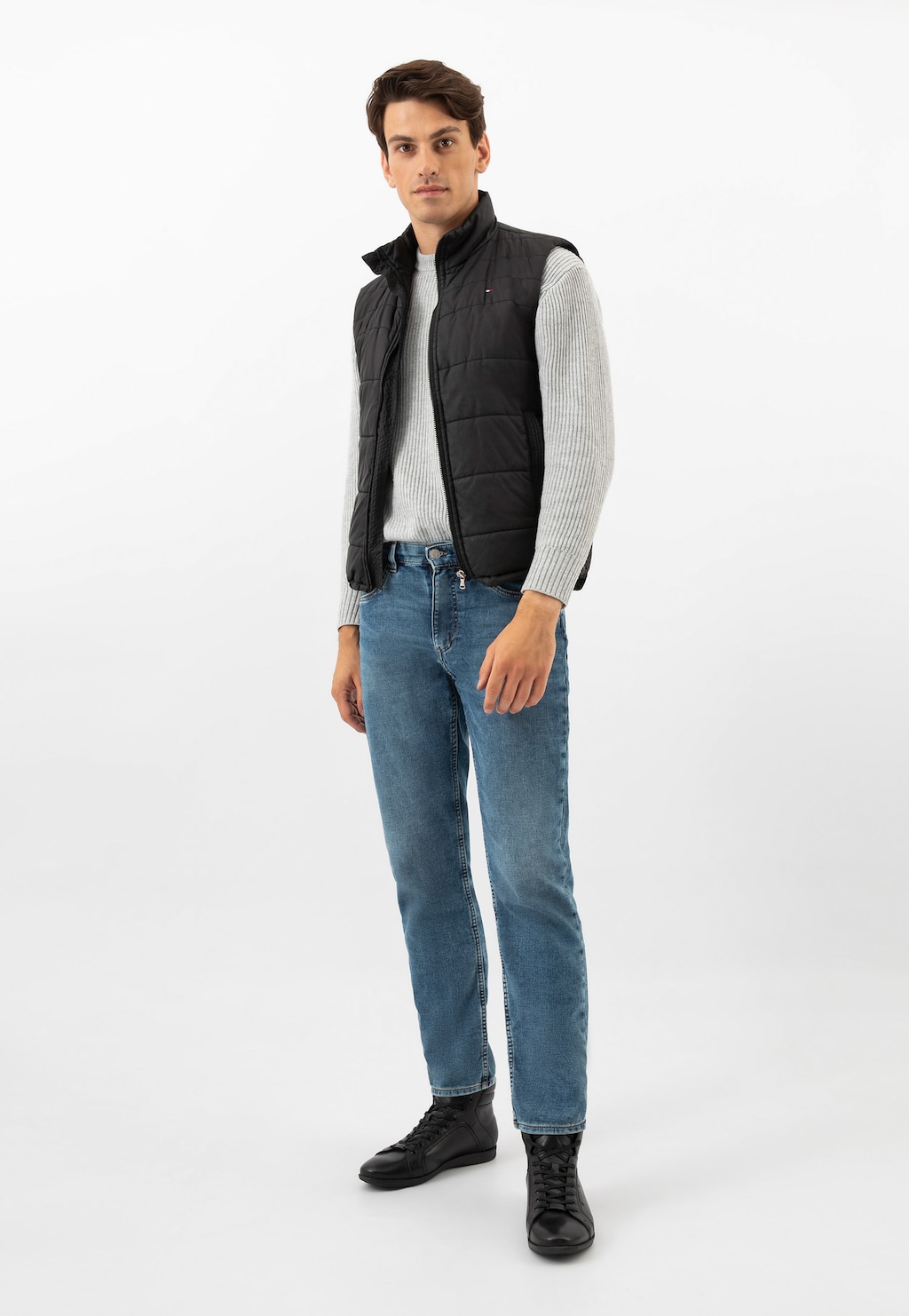 Model prezentujący czarne trzewiki męskie Wojas 24093-51 w stylizacji z czarną pikowaną kamizelką, szarym swetrem i niebieskimi jeansami.