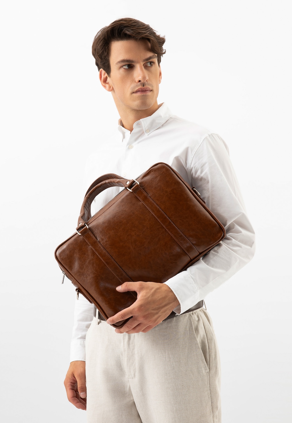 Elegancka brązowa torba skórzana Wojas 80074-53 z przegrodą na laptopa, trzymana przez modela w białej koszuli i jasnych spodniach. Idealna na biznesowe spotkania.