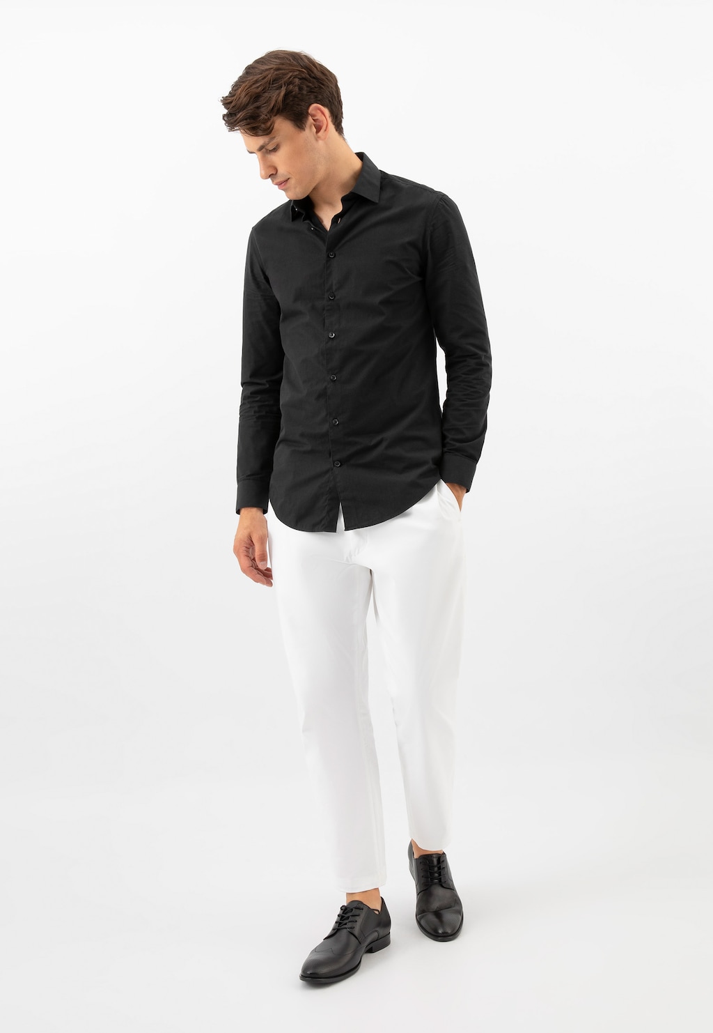 Model w eleganckim stroju prezentuje czarne buty męskie Wojas 10195-51 ze skóry licowej. Stylizacja z czarną koszulą i białymi spodniami podkreśla formalny charakter obuwia.