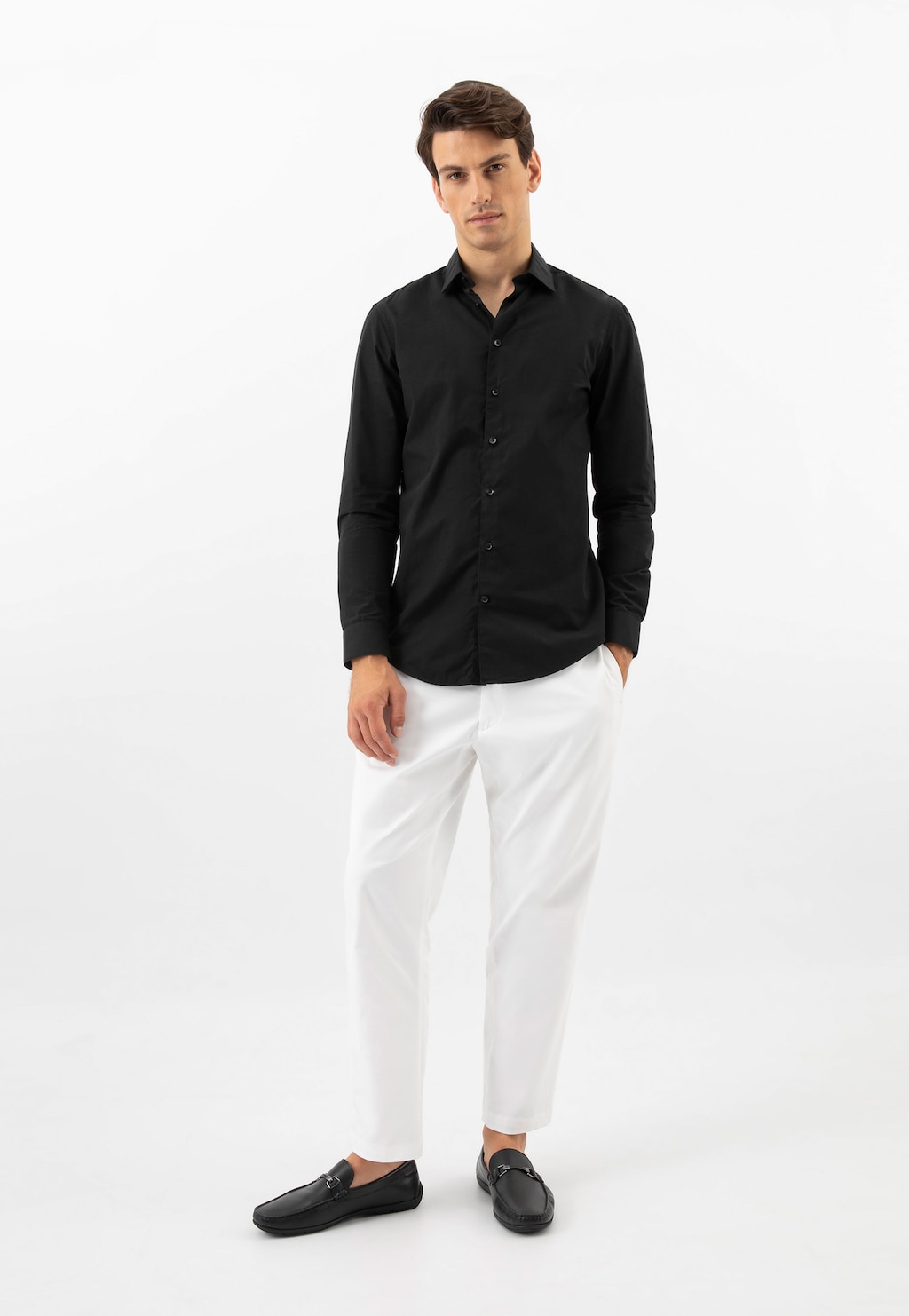 Model w eleganckim stroju: czarna koszula, białe spodnie i czarne mokasyny Wojas model 10200-51 z ozdobą. Stylowa kompozycja męskiej odzieży i obuwia.