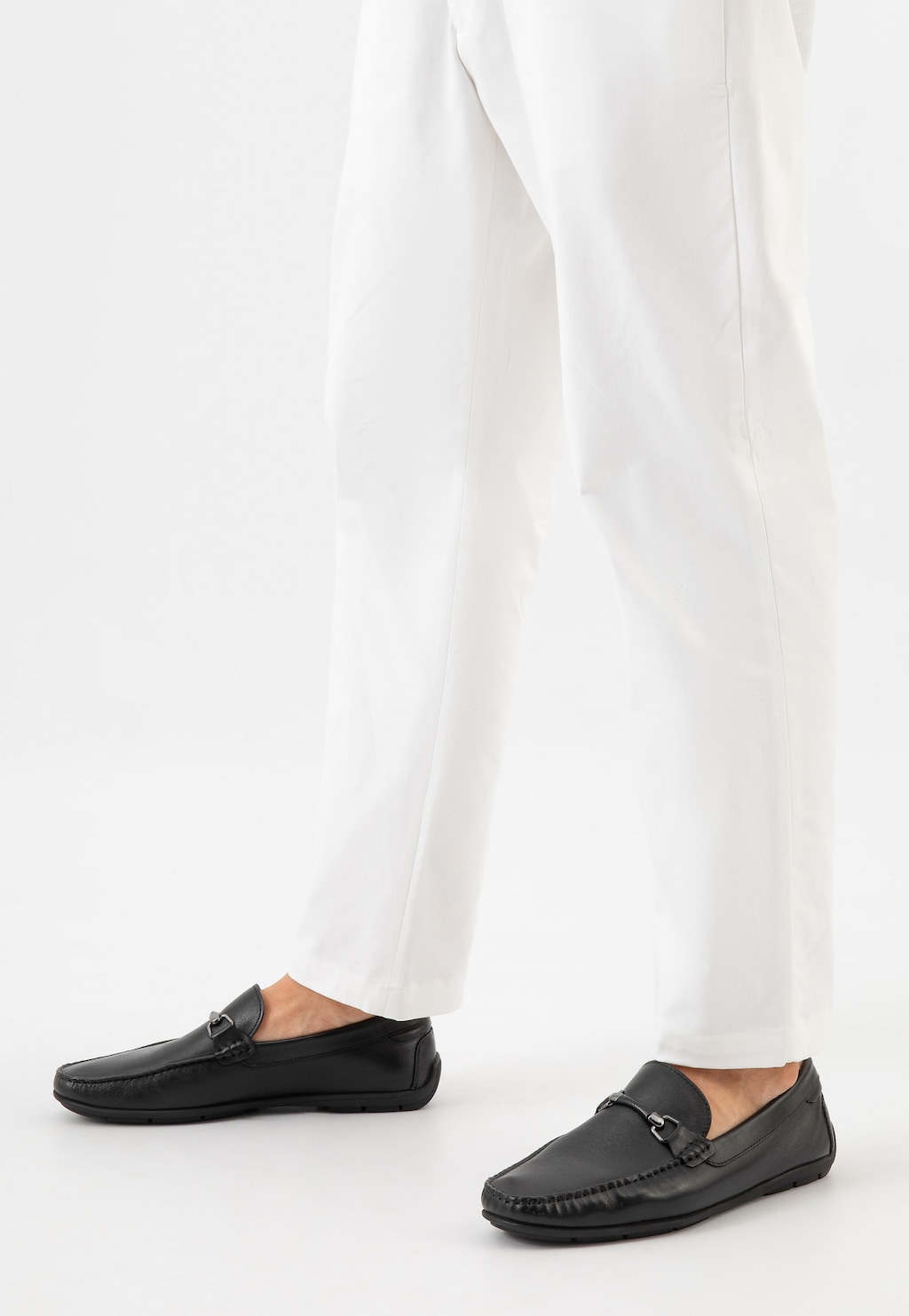 Czarne skórzane mokasyny męskie Wojas model 10200-51 z metalową ozdobą noszone do białych spodni. Widok z boku ukazujący elegancki profil obuwia.