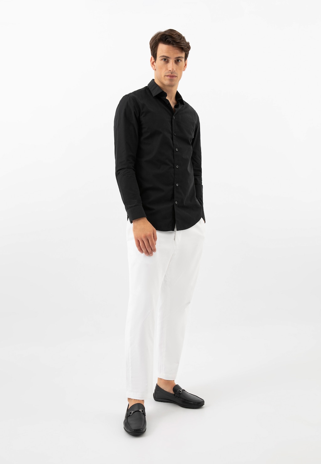 Model w eleganckiej stylizacji z czarną koszulą i białymi spodniami, prezentujący czarne skórzane mokasyny męskie Wojas z ozdobą, model 10200-51.