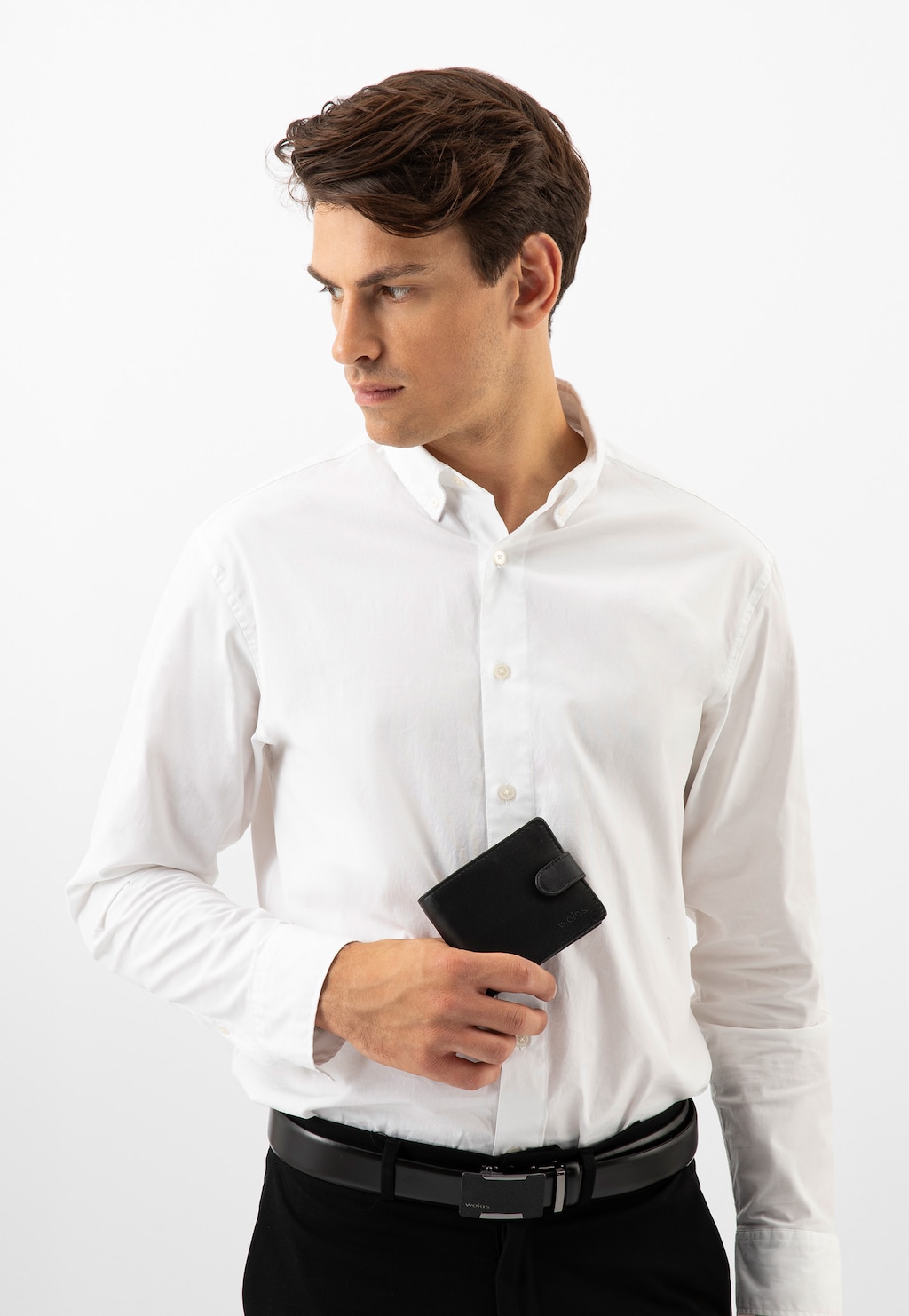 Mężczyzna w białej koszuli trzymający czarny portfel męski Wojas model 91047-51 zapinany na zatrzask. Elegancki look uzupełniony czarnymi spodniami i paskiem.