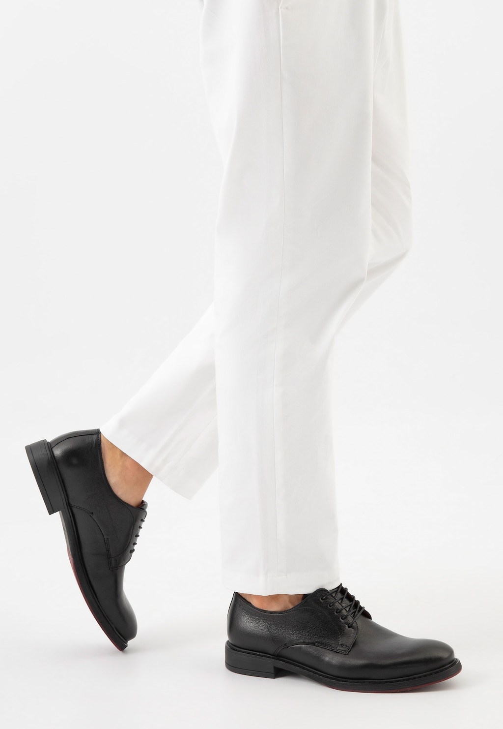 Eleganckie czarne półbuty Wojas 10226-51 ze skóry licowej na nogach osoby w białych spodniach, ukazane z profilu. Klasyczny wizytowy model męski ze sznurowaniem.