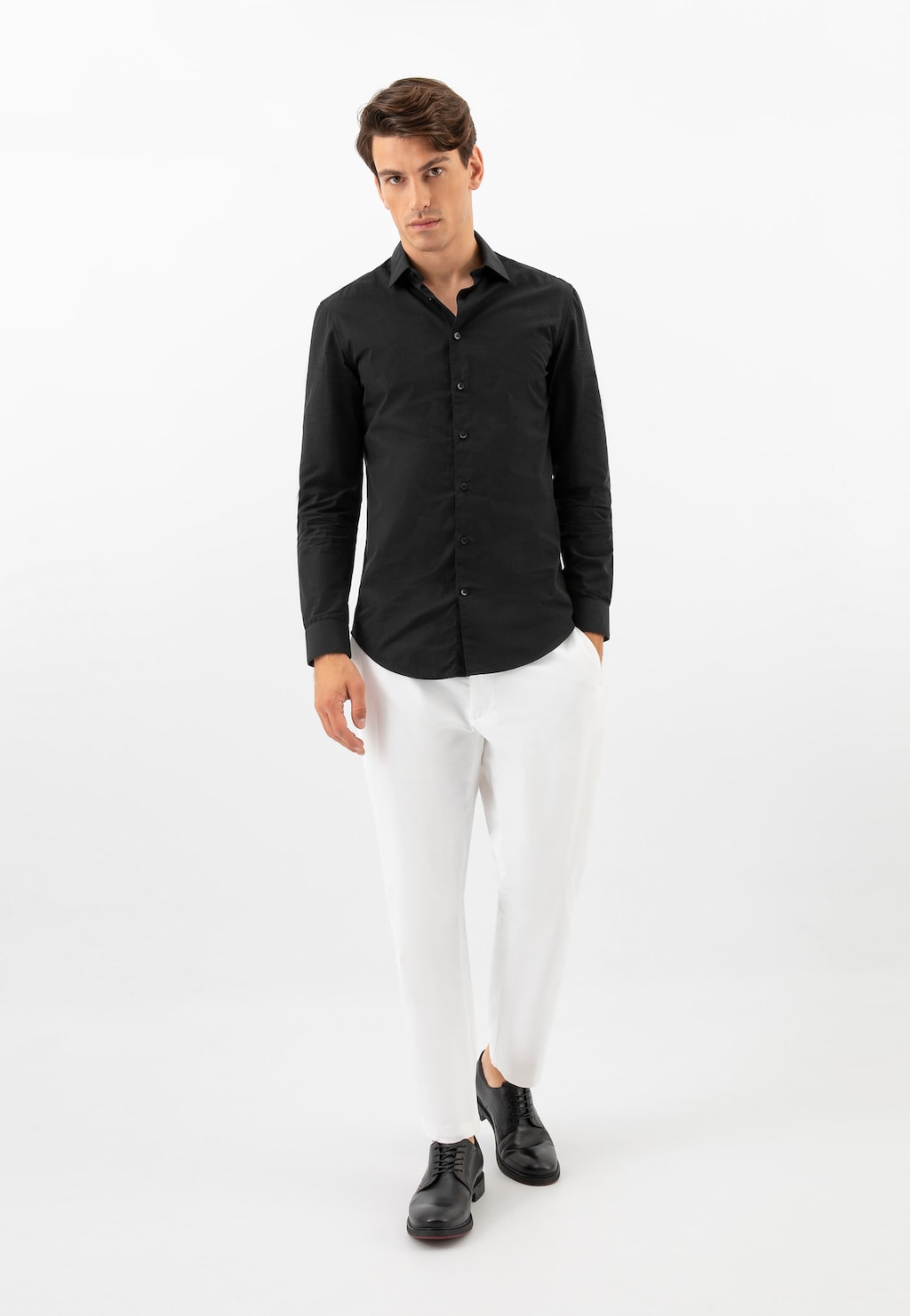 Model w eleganckim stroju z czarną koszulą i białymi spodniami, prezentujący czarne wizytowe półbuty męskie Wojas ze skóry licowej model 10226-51 widoczne na stopach.