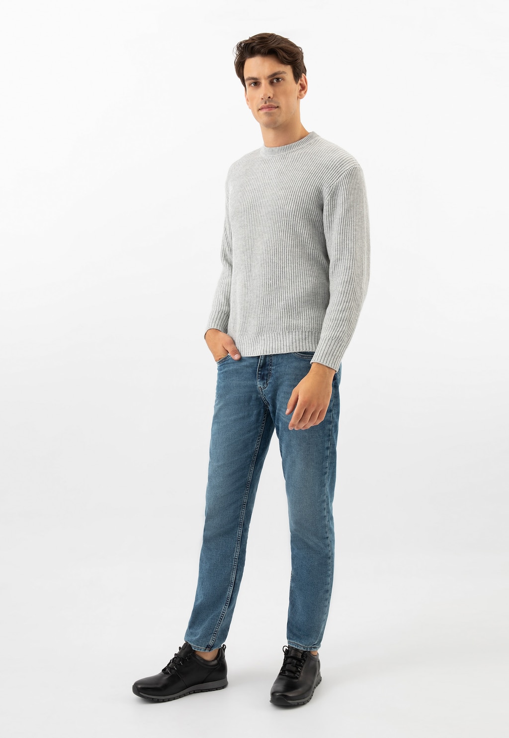 Model w szarym swetrze i niebieskich jeansach prezentuje czarne sneakersy Wojas model 10039-51 ze skóry licowej, widoczne z przodu, idealne do casualowych stylizacji.