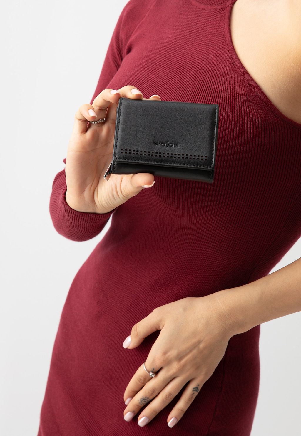 Elegancki czarny portfel Wojas model 91067-71 z ochroną RFID i czerwonym wnętrzem, trzymany w dłoni przez osobę w bordowej sukience.