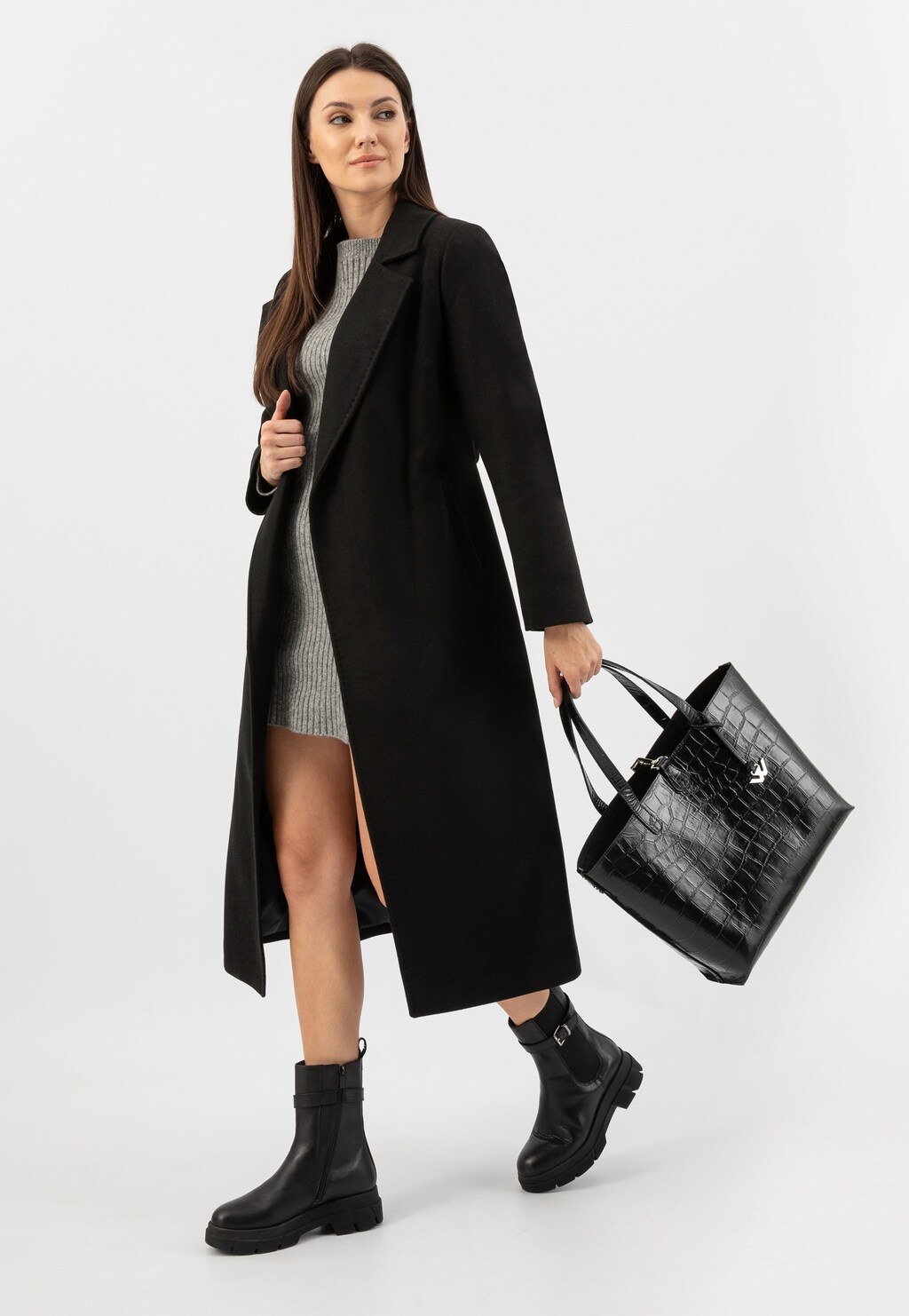 Modelka w czarnym płaszczu i szarej sukience, trzymająca dużą torebkę Wojas 80250-81 z tłoczeniem w zwierzęcy print. Stylizację uzupełniają czarne botki marki Wojas.