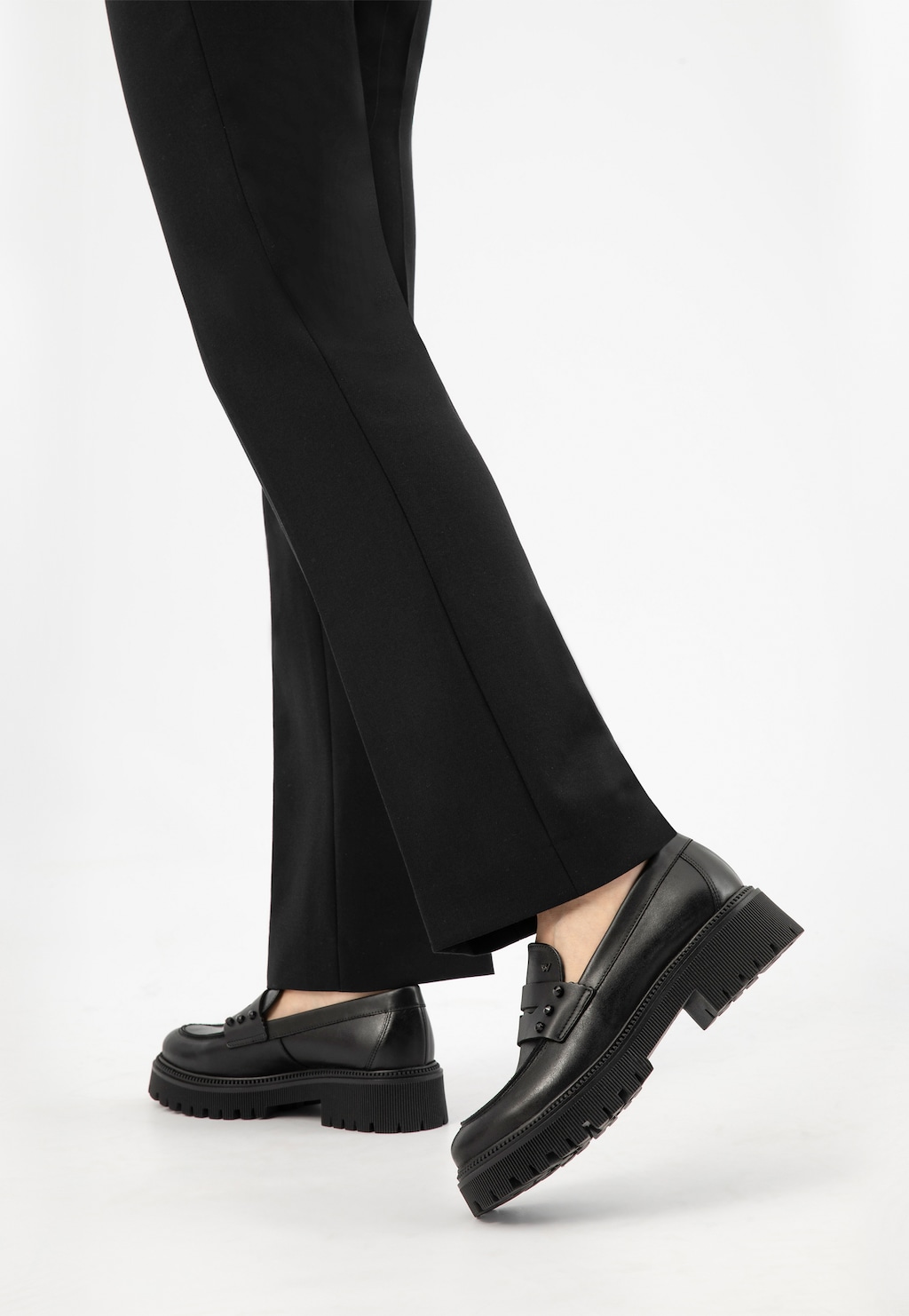 Eleganckie czarne skórzane mokasyny Wojas model 46311-51 penny loafers noszone do czarnych spodni. Widok z boku ukazujący masywną podeszwę i klasyczny fason buta.