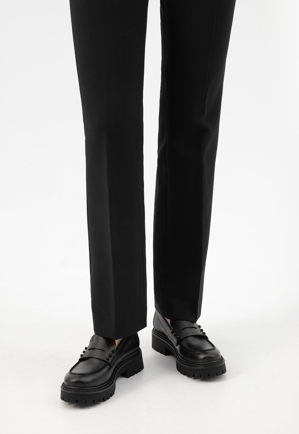 Czarne skórzane mokasyny penny loafers Wojas model 46311-51 w stylizacji z eleganckimi spodniami, ukazane z perspektywy stóp. Buty mają grubą, profilowaną podeszwę.