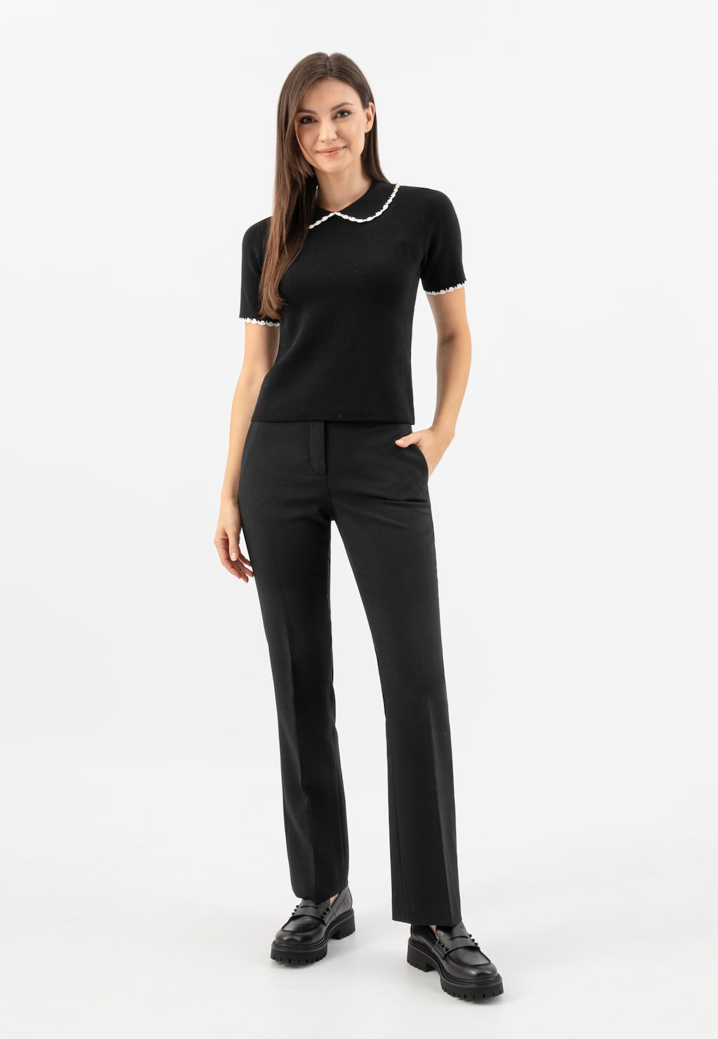 Elegancki czarny strój składający się z bluzki z białym kołnierzykiem i spodni. Na nogach widoczne czarne skórzane mokasyny penny loafers Wojas model 46311-51.