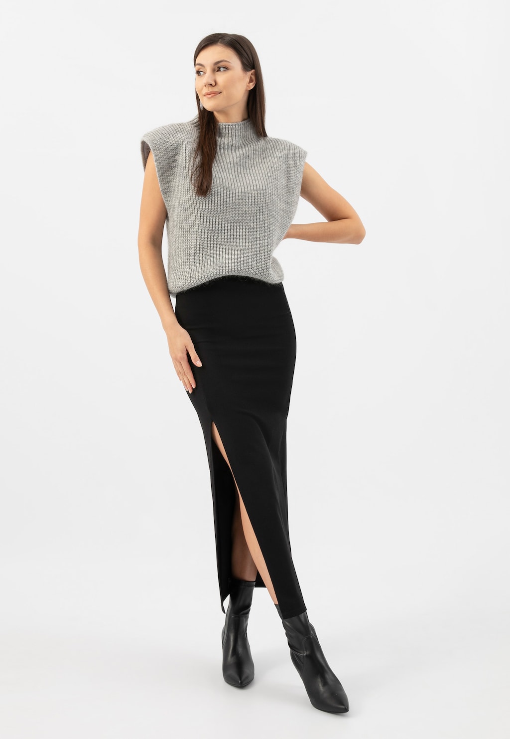 Modelka w szarym swetrze bez rękawów i czarnej spódnicy z rozcięciem, prezentująca czarne eleganckie botki Wojas na szpilce model 55017-51, idealne do stylizacji biznesowych.