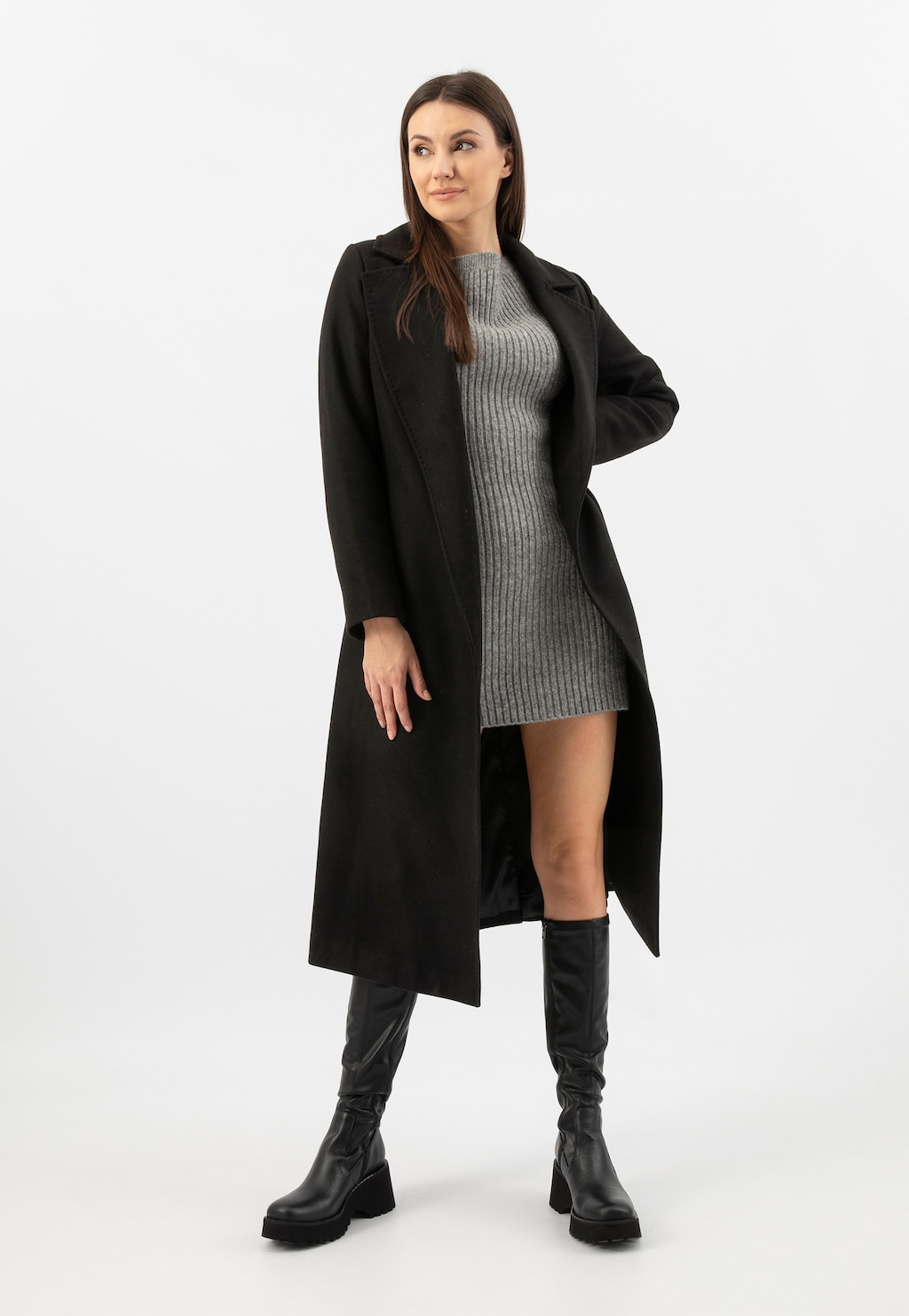 Modelka w szarej sukience i czarnym płaszczu prezentuje czarne kozaki Wojas model 71065-81 na platformie. Eleganckie buty jesienne z wysoką cholewką, idealne do jesiennych stylizacji.