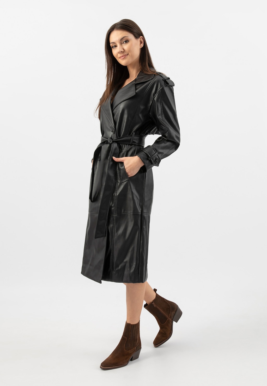 Modelka w czarnym skórzanym płaszczu prezentująca brązowe botki typu kowbojki Wojas model 55294-62, widok całej sylwetki, strój uzupełniony o brązowe botki z charakterystycznym kowbojskim profilem.