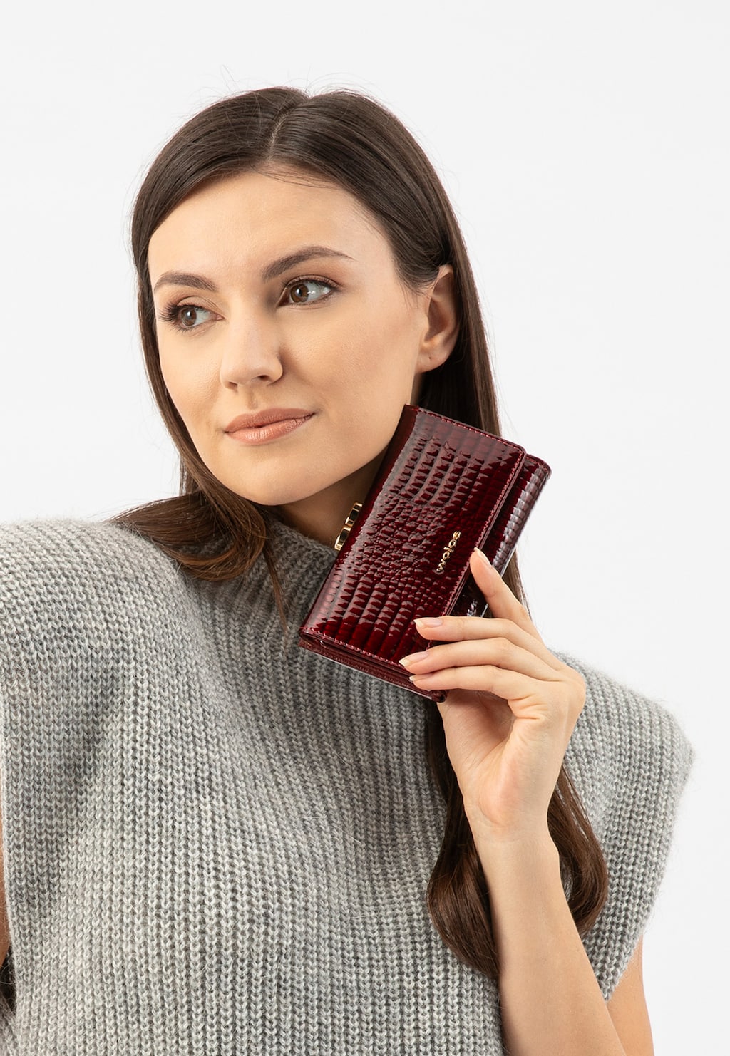 Czerwony lakierowany portfel Wojas model 91085-35 z wieloma przegrodami, trzymany w dłoni. Osoba w szarym dzianinowym topie prezentuje produkt.