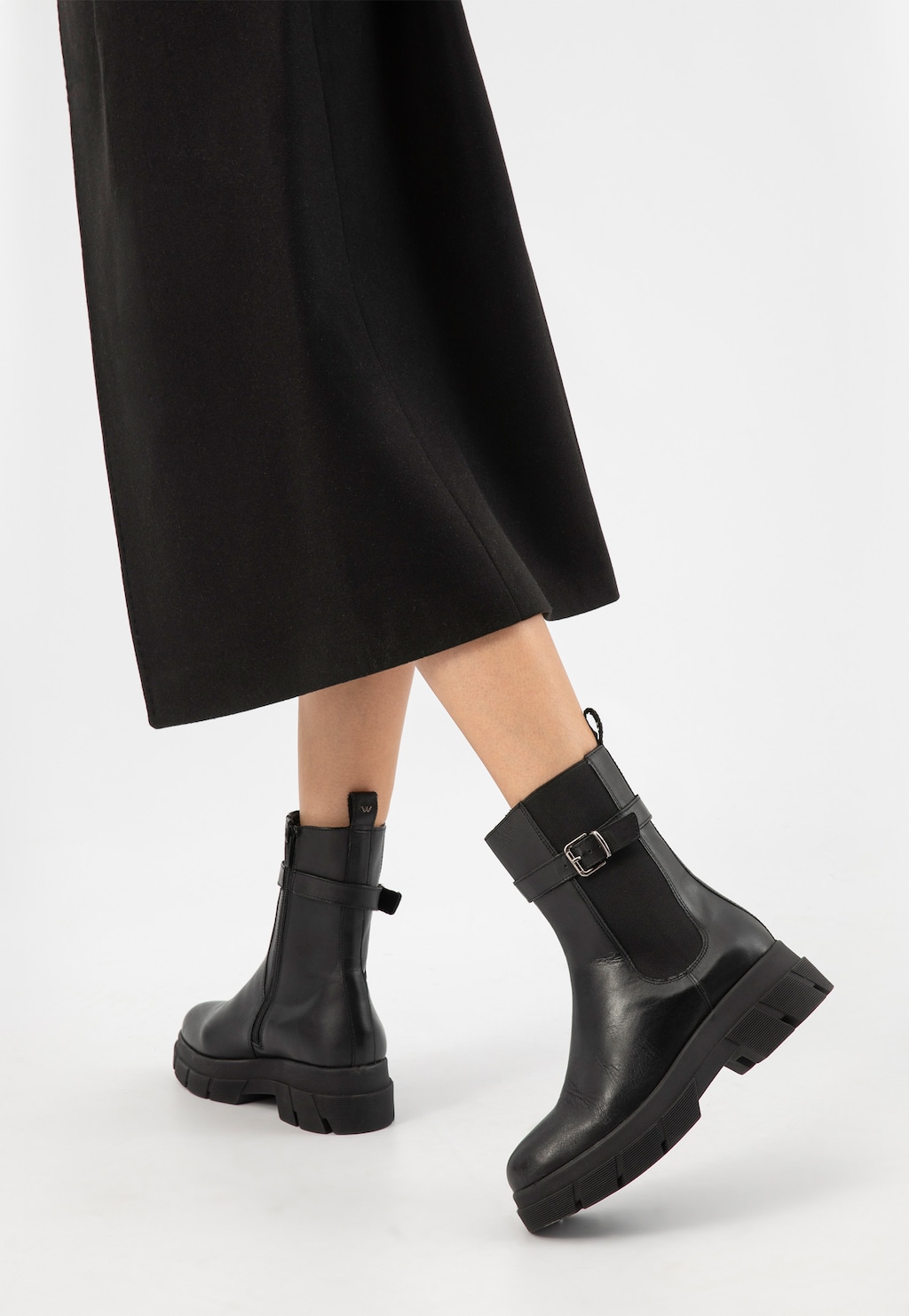 Czarne skórzane botki damskie Wojas 55189-51 z ozdobną klamerką, na grubej podeszwie, noszone do długiej czarnej spódnicy, widok z tyłu.