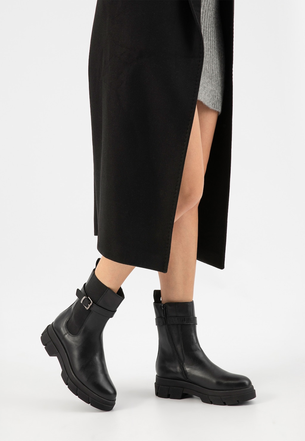 Czarne skórzane botki damskie Wojas 55189-51 z ozdobną klamerką, zaprezentowane na nogach modelki w czarnej spódnicy z rozcięciem, na masywnej podeszwie.