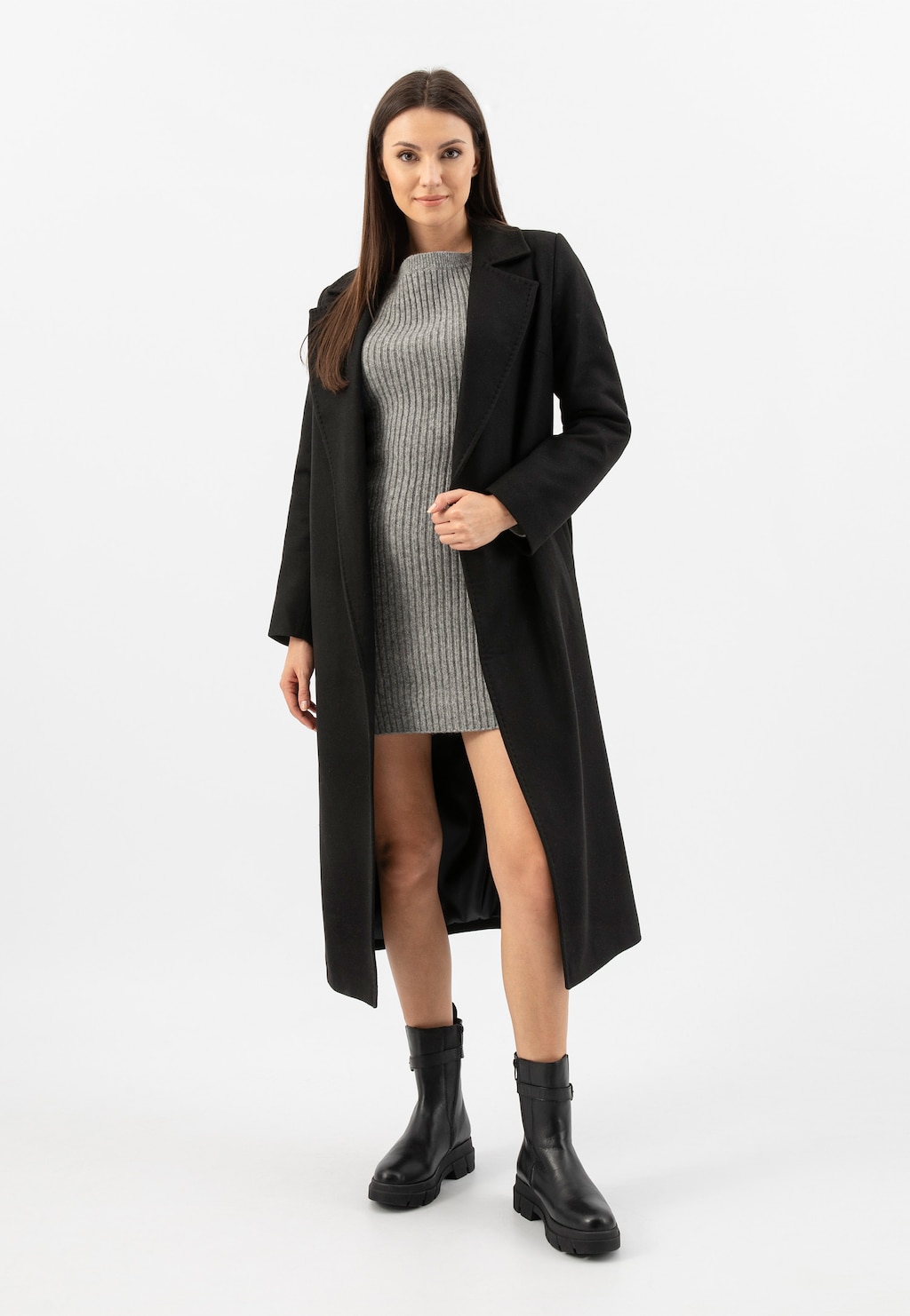 Modelka w czarnym płaszczu i szarej sukience, prezentująca czarne skórzane botki damskie Wojas model 55189-51 z ozdobną klamerką - eleganckie obuwie na platformie.