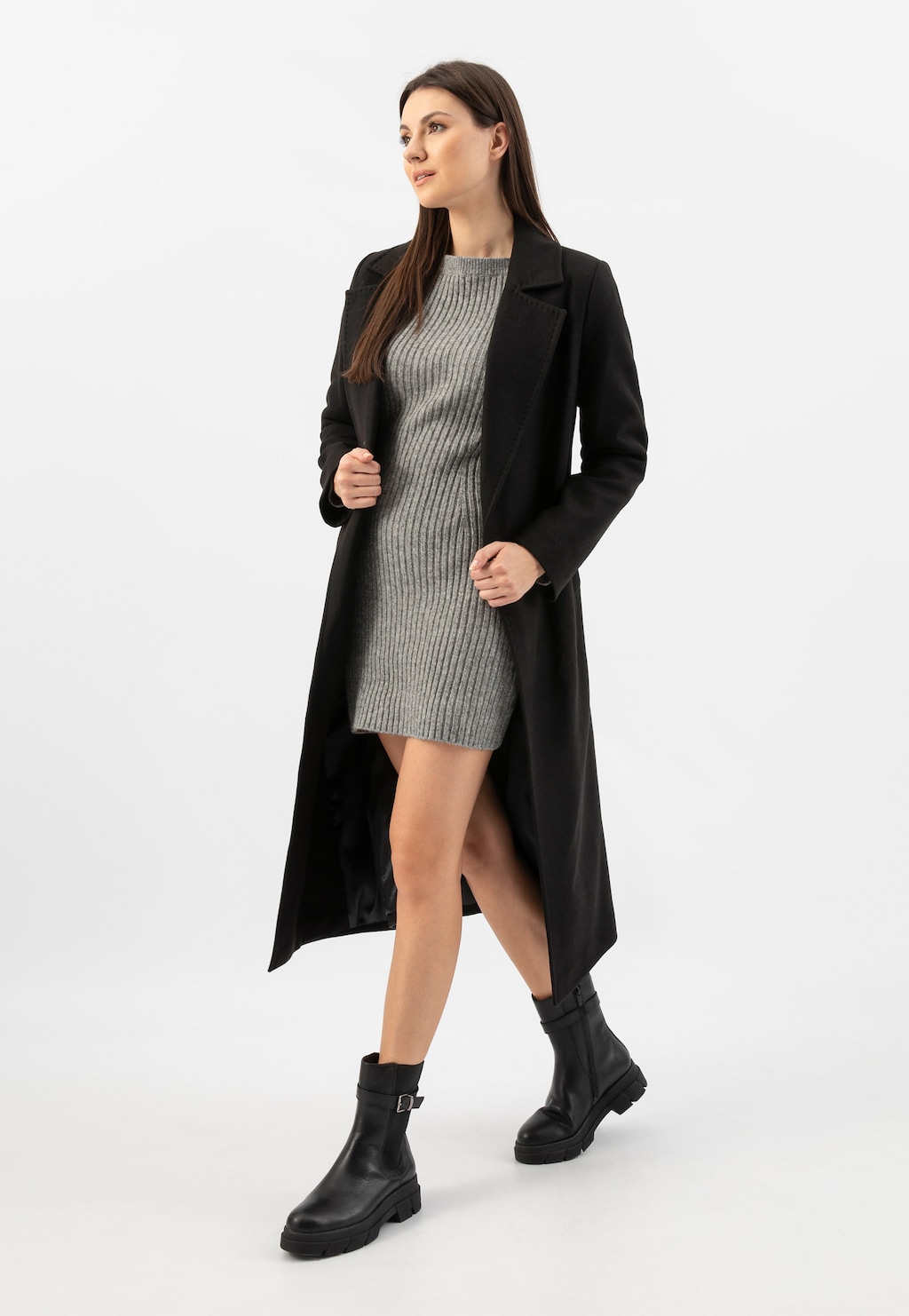 Modelka w czarnym płaszczu i szarej sukience prezentuje czarne skórzane botki damskie Wojas model 55189-51 z ozdobną klamerką, idealne do jesiennych stylizacji.