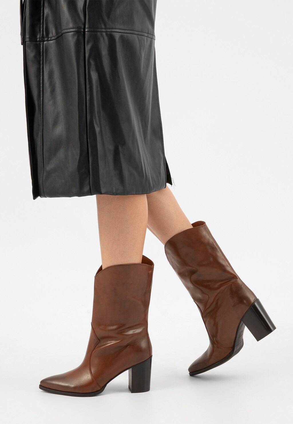 Brązowe kowbojki damskie Wojas 55239-52 ze skóry naturalnej na stabilnym obcasie, noszone z czarną skórzaną spódnicą. Elegancki model z charakterystycznym szpiczastym noskiem.