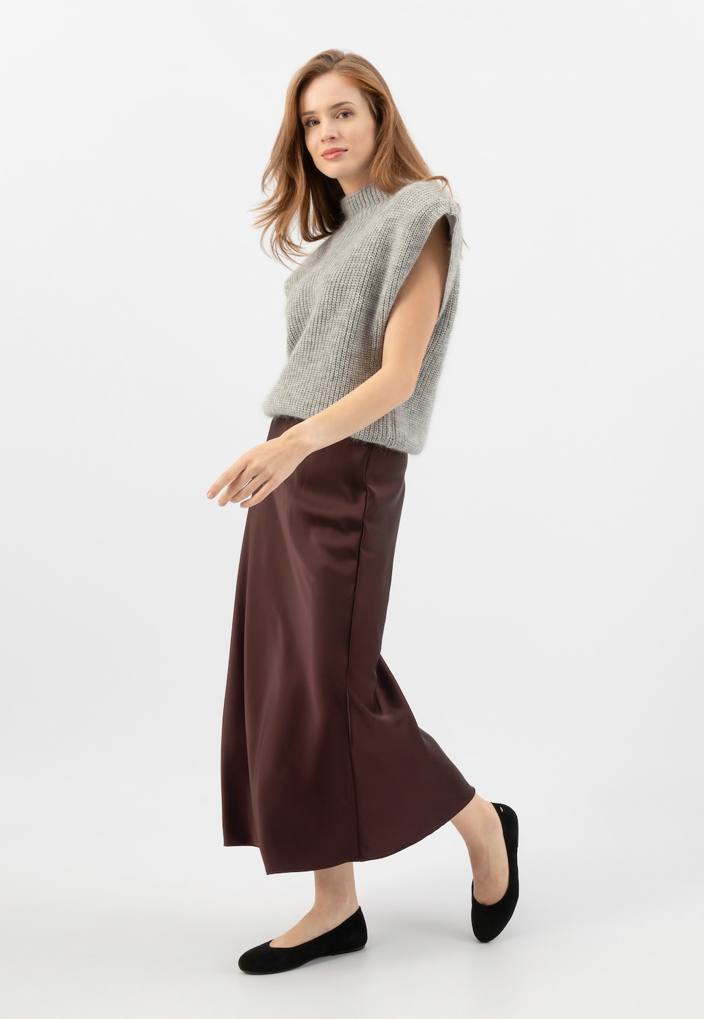 Modelka w szarym swetrze bez rękawów i brązowej spódnicy midi prezentująca czarne welurowe baleriny Wojas model 44024-61 z zaokrąglonym noskiem.