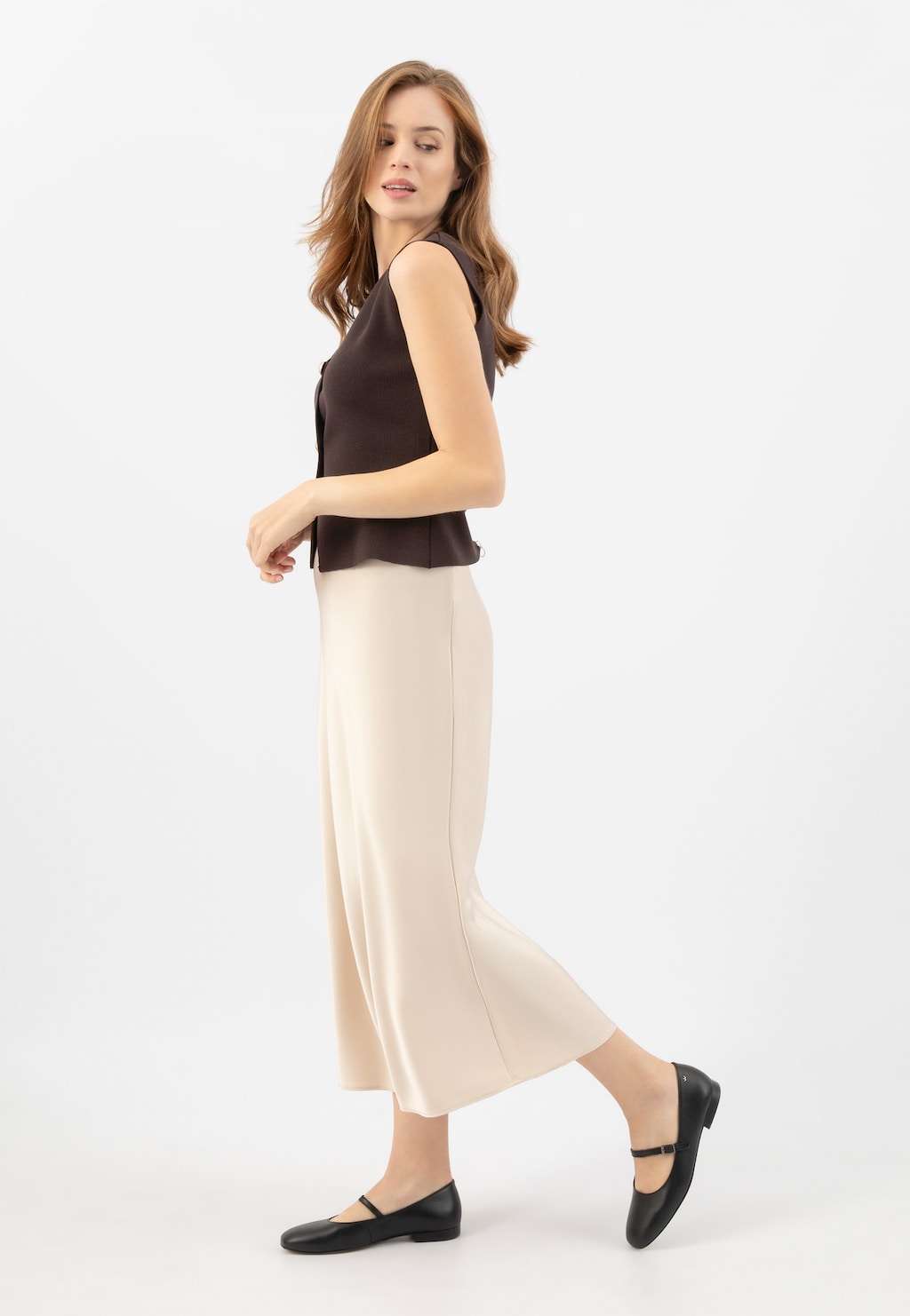 Modelka w eleganckim stroju z długą kremową spódnicą, prezentująca czarne skórzane baleriny Wojas model 44029-51 z charakterystycznym paskiem na podbiciu.
