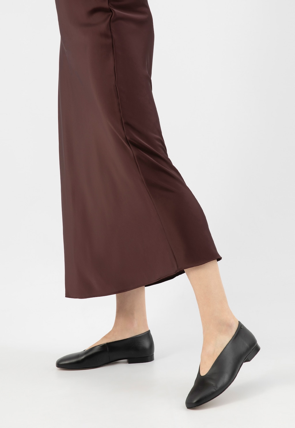 Eleganckie czarne skórzane baleriny Wojas model 44030-51 na stopach osoby w brązowej spódnicy midi, ukazane z profilu, podkreślające klasyczny i minimalistyczny styl.