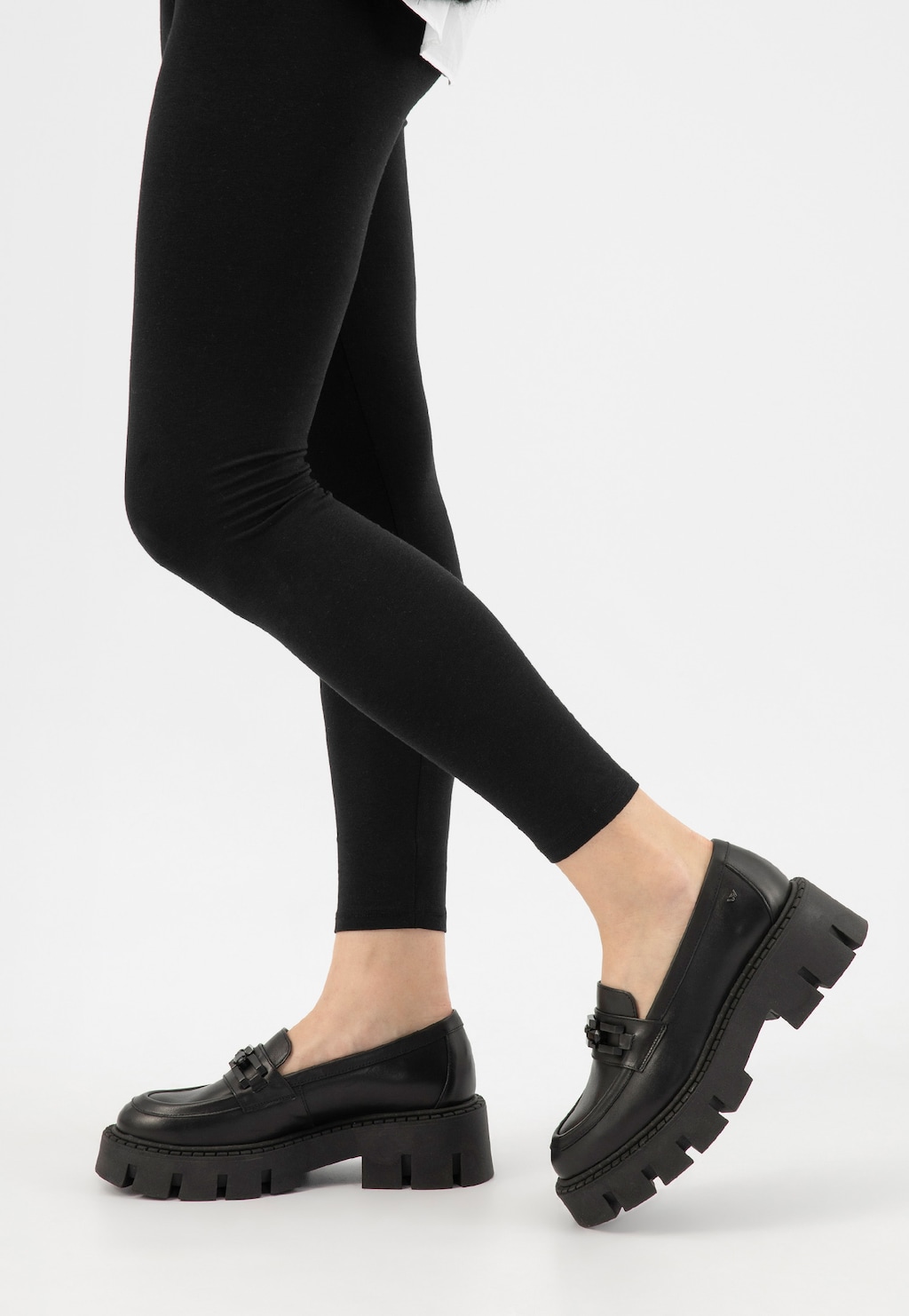 Czarne masywne mokasyny Wojas model 46317-51 z charakterystycznym łańcuchem na podbiciu i grubą podeszwą, noszone do czarnych legginsów, widok z boku.