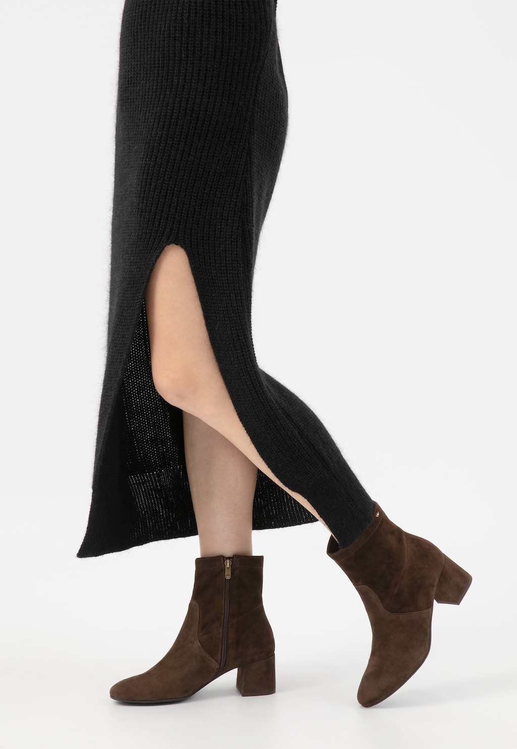 Brązowe jesienne botki Wojas model 55094-62 na niskim obcasie prezentowane na nodze w czarnej dzianinowej spódnicy z rozcięciem. Stylowe obuwie o zamszowej fakturze.