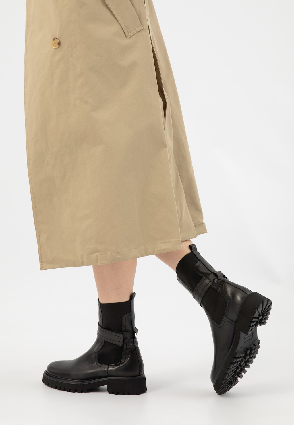 Eleganckie czarne sztyblety Wojas model 55279-51 ze skóry licowej pokazane na nogach osoby w beżowym płaszczu. Buty mają wyrazisty wzór podeszwy i masywny charakter.