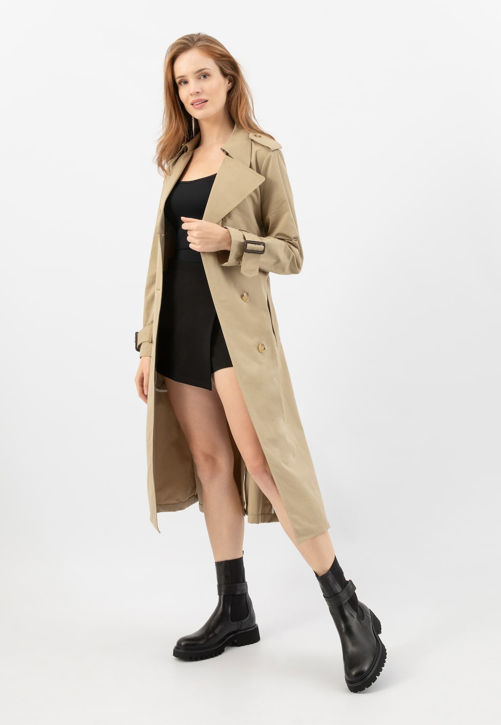 Modelka w beżowym trenczu i czarnej sukience prezentuje wysokie sztyblety damskie Wojas model 55279-51 ze skóry licowej. Eleganckie buty o czarnym kolorze z masywną podeszwą.