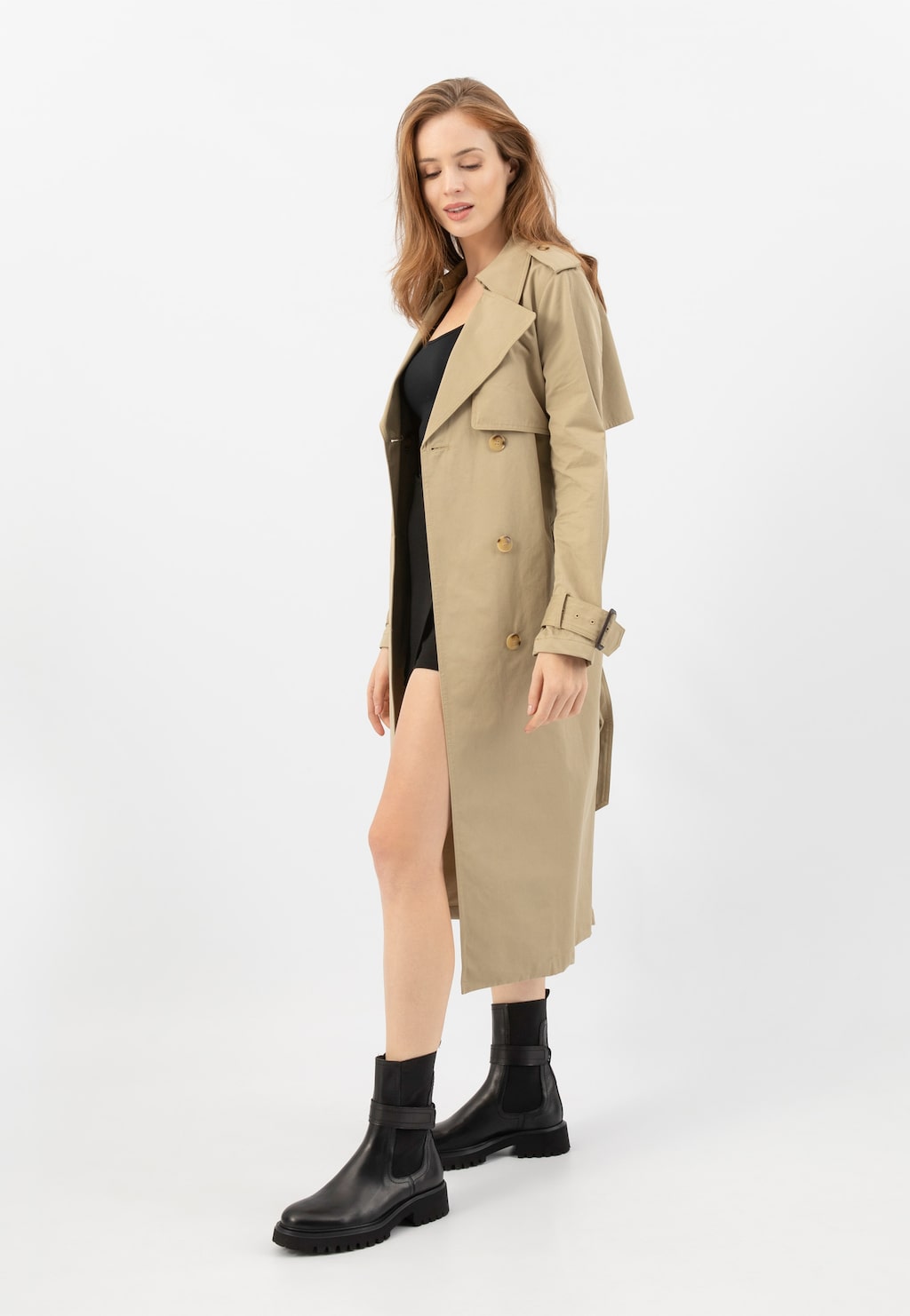 Modelka w beżowym trenczu i czarnej sukience prezentująca czarne wysokie sztyblety Wojas model 55279-51 ze skóry licowej, doskonale uzupełniające elegancką stylizację.