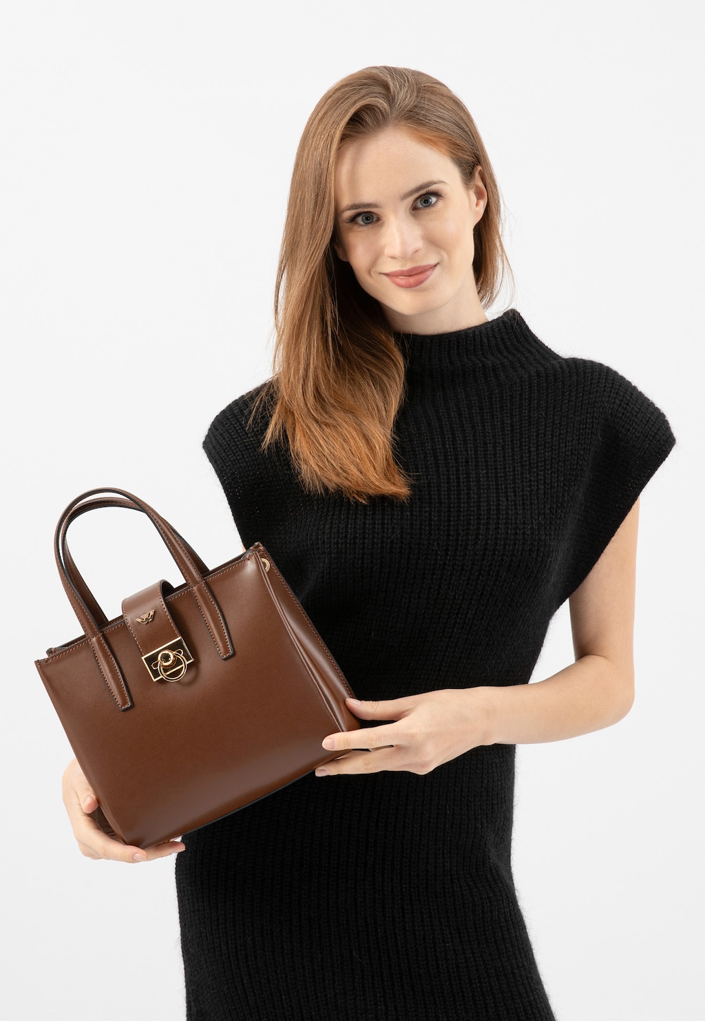 Elegancka ciemnobrązowa torebka damska Wojas typu kuferek model 80404-52 prezentowana w ręku, na tle czarnej dzianinowej sukienki bez rękawów.
