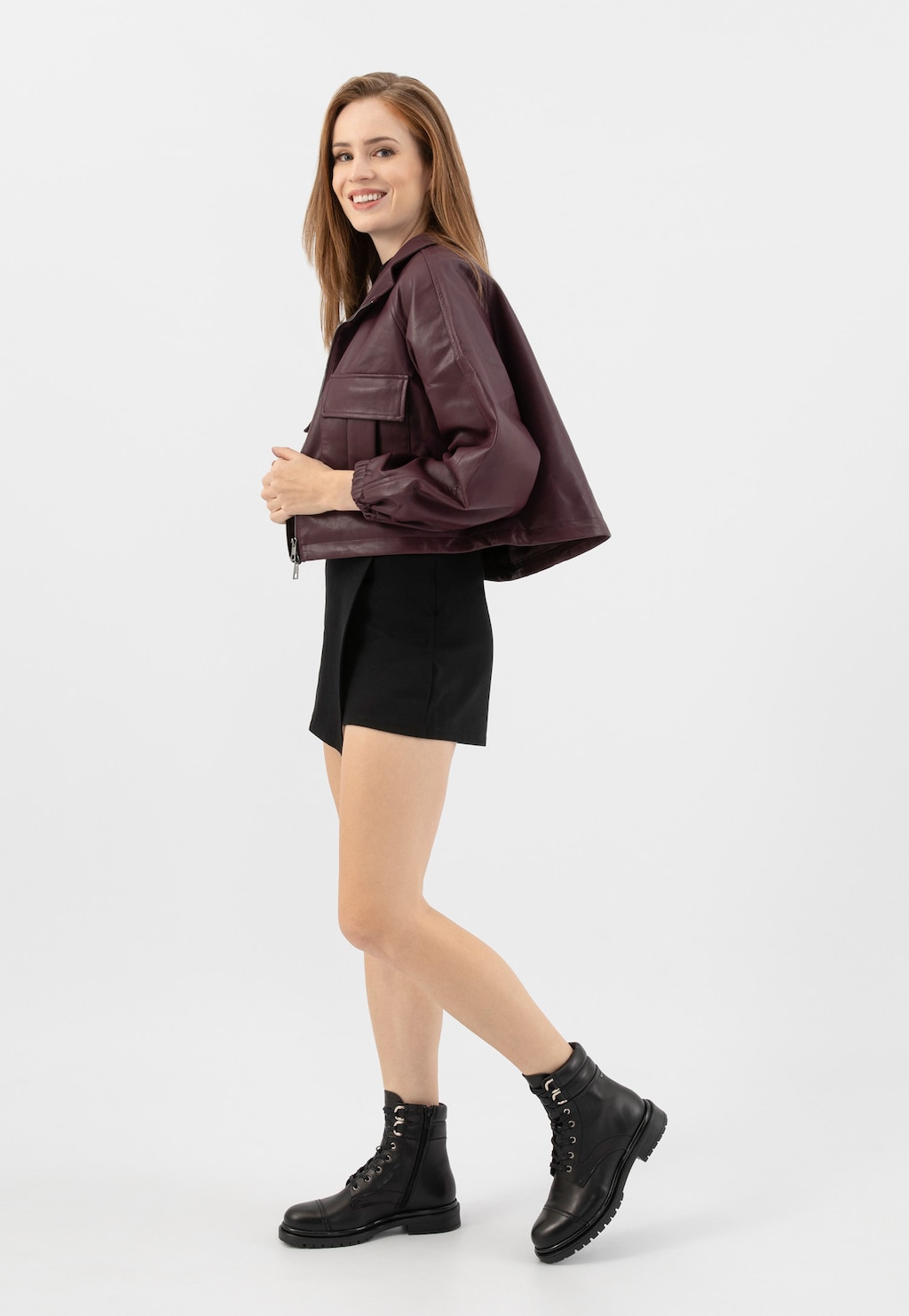 Modelka w bordowej skórzanej kurtce i czarnej spódnicy, prezentująca czarne skórzane trzewiki Wojas model 64129-51 ze sznurowadłami i zamkiem, widoczne w pełnej stylizacji.