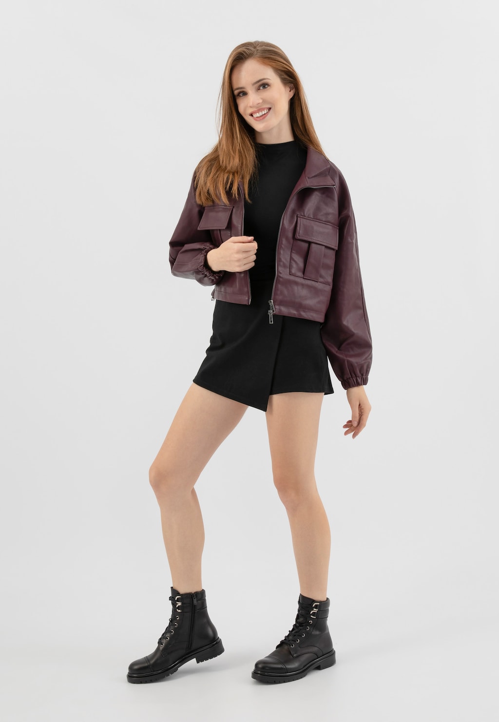 Modelka w czarnej sukience i bordowej kurtce prezentuje czarne skórzane trzewiki Wojas model 64129-51 ze sznurowadłami i zapięciem na zamek, idealne do stylizacji miejskich.