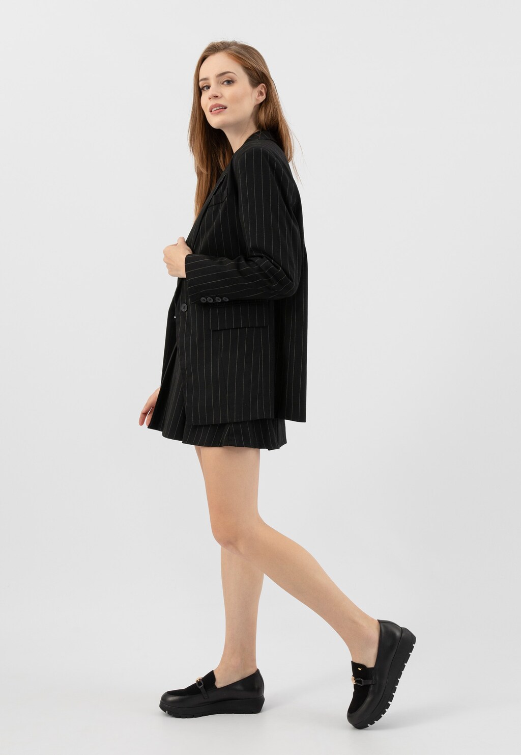 Modelka w czarnym garniturze w paski prezentuje półbuty damskie Wojas model 46304-71 wykonane z łączonych czarnych skór, idealne do eleganckiej stylizacji.