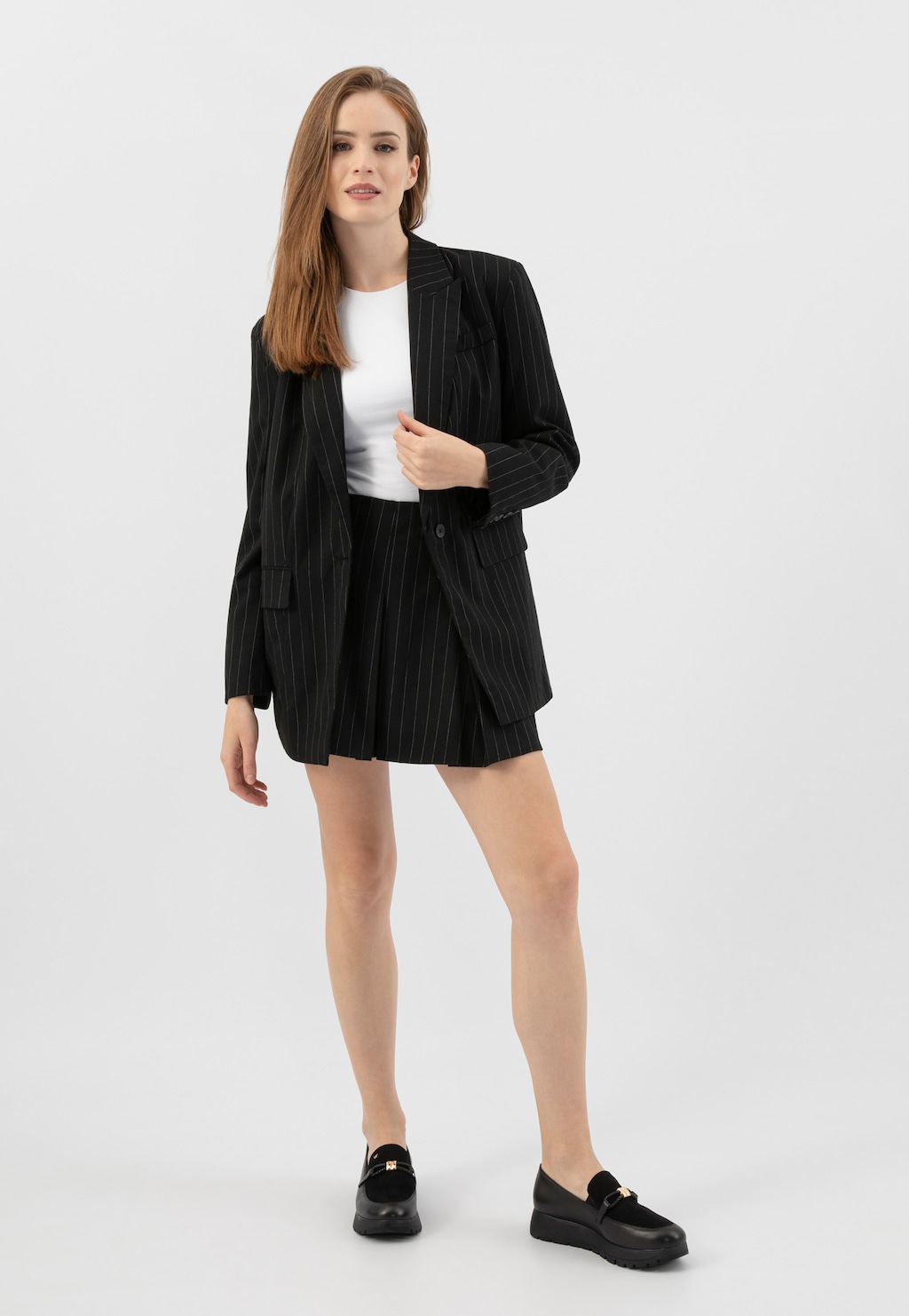 Modelka w czarnym garniturze w paski i białej bluzce, prezentująca czarne półbuty damskie Wojas model 46304-71 z łączonych skór, idealne do eleganckiej stylizacji.