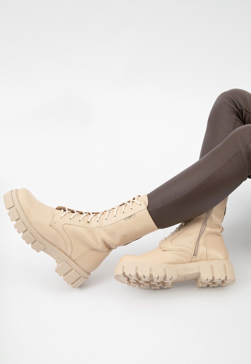 Beżowe trzewiki damskie Wojas 64020-54 typu bikery z masywną podeszwą, zaprezentowane na nogach w brązowych spodniach, z bocznym zamkiem i sznurowaniem.