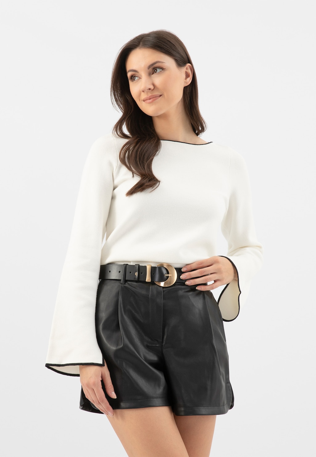 Modelka w białej bluzce z czarnymi szortami, prezentująca czarny skórzany pasek damski Wojas z dużą klamrą model 93089-51, podkreślający elegancką stylizację.