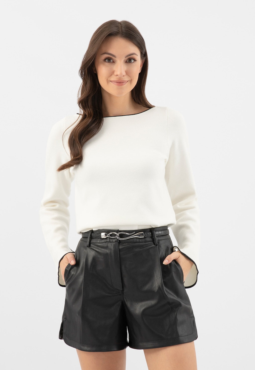 Elegancki czarny pasek Wojas model 93095-51 z oryginalną klamrą, prezentowany na krótkich czarnych spodniach ze skóry, zestawiony z białą bluzką z długim rękawem.