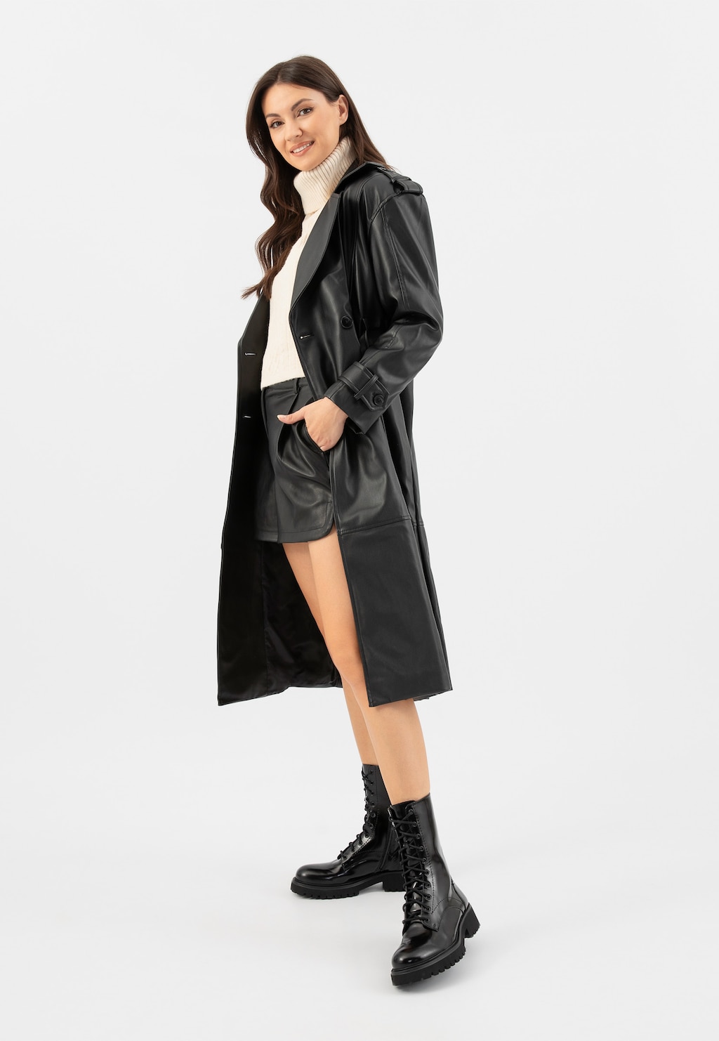Modelka w czarnym płaszczu skórzanym i kremowym golfie prezentuje wysokie lakierowane trzewiki damskie Wojas model 64128-31 w stylu militarnym z charakterystycznymi sznurowaniami.