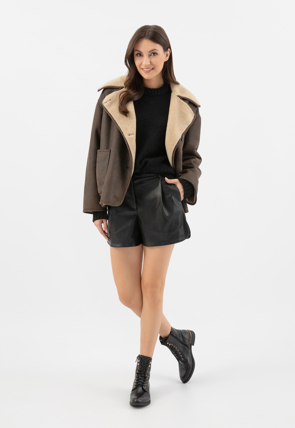 Stylizacja zimowa z czarnymi skórzanymi trzewikami Wojas 64127-51 ze złotymi elementami, uzupełniona brązową kurtką z kożuszkiem, czarnym swetrem i skórzanymi szortami.
