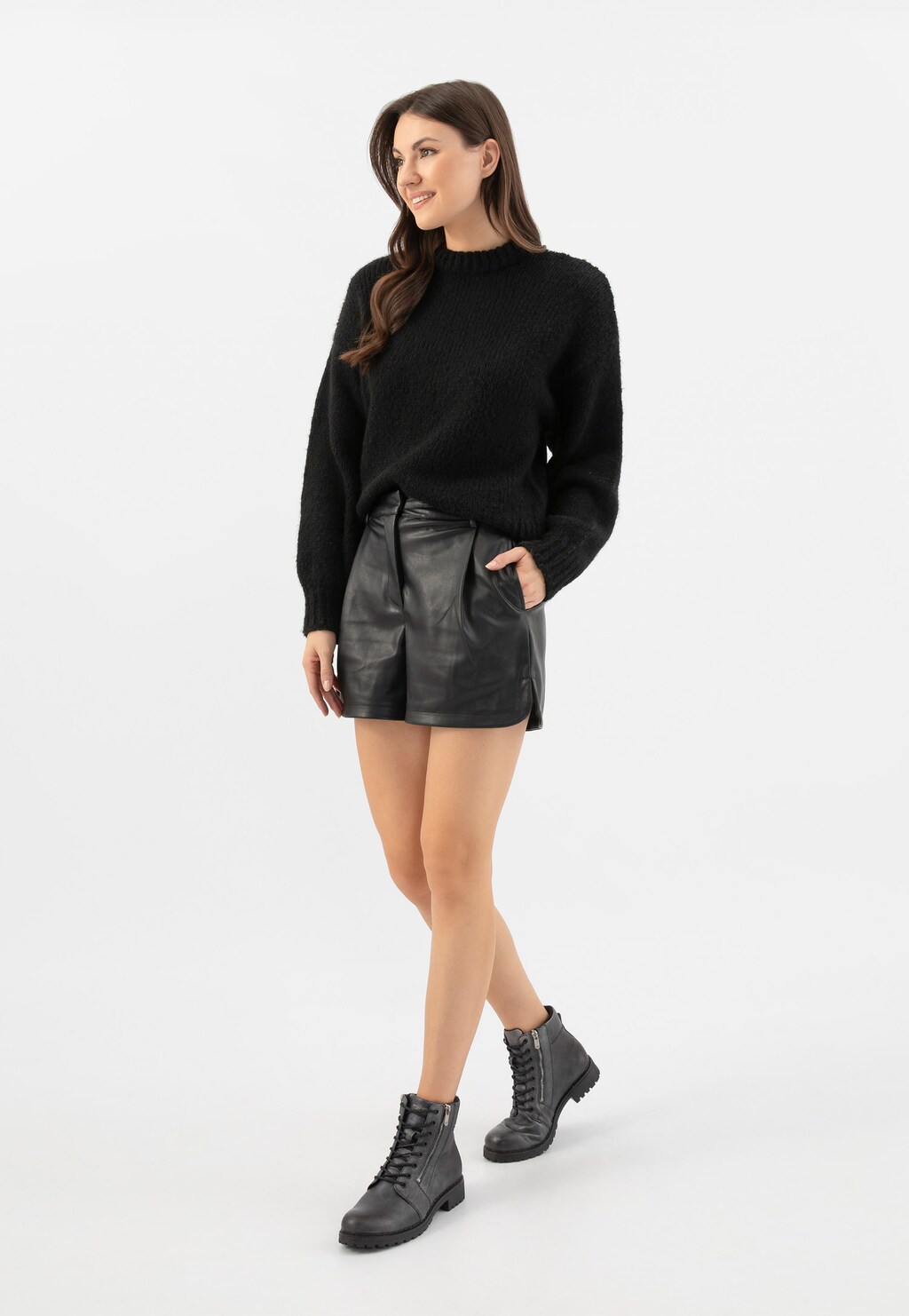 Modelka w czarnym swetrze i skórzanych szortach prezentuje trzewiki Wojas typu workery model 64076-59 w kolorze ciemnego srebra, ukazane z profilu na nogach.