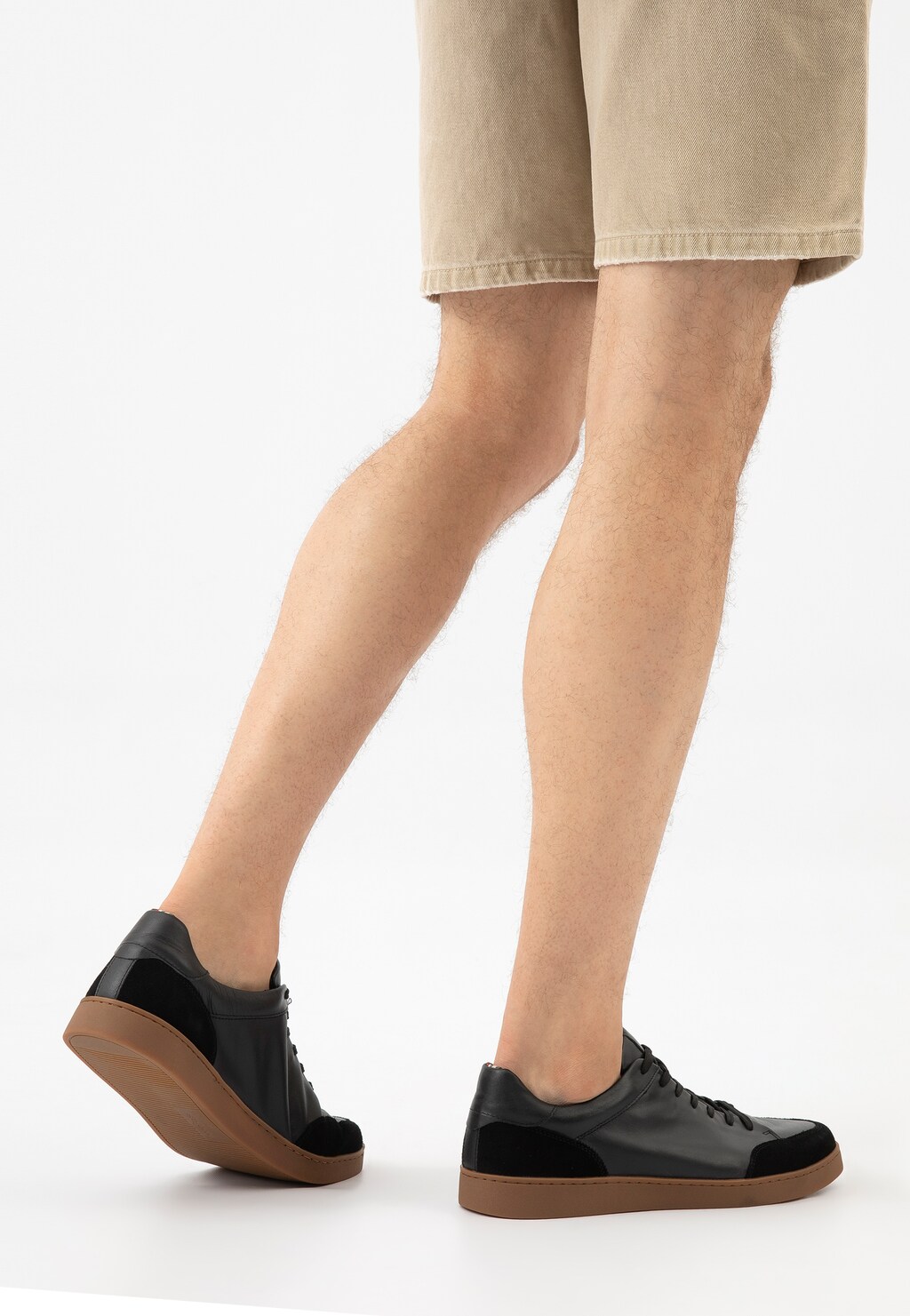 Czarne trampki Wojas 10217-51 z łączonych skór na brązowej podeszwie, prezentowane na nogach osoby w beżowych szortach, widok z profilu.