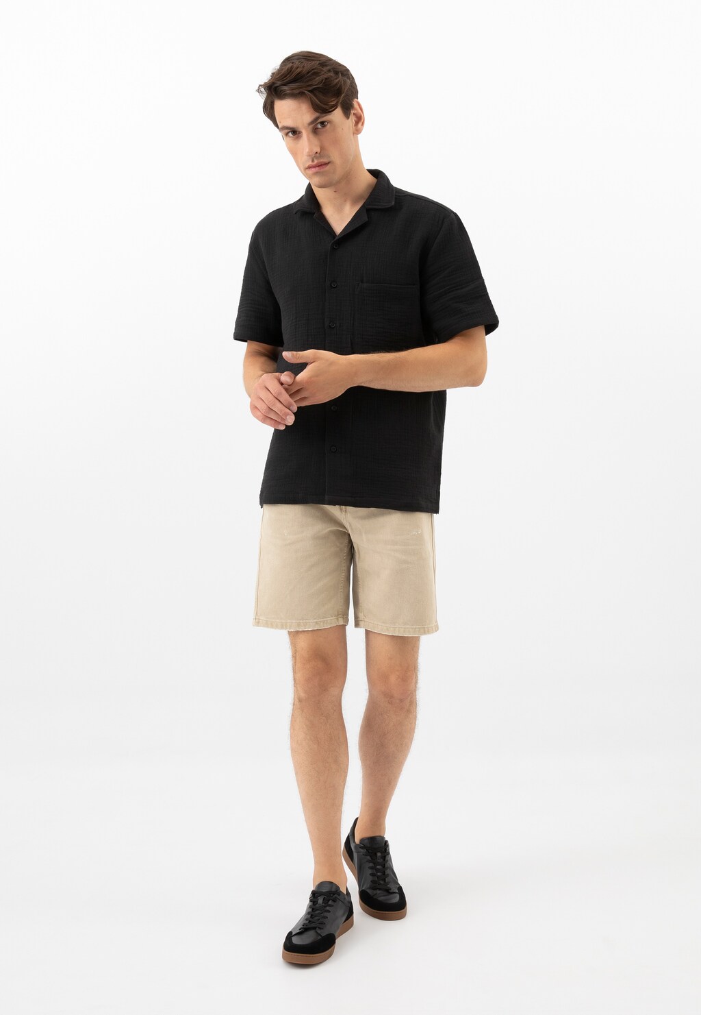 Model w czarnej koszulce i beżowych szortach prezentuje czarne trampki Wojas model 10217-51 z łączonych skór na brązowej podeszwie, ukazane w pełnej stylizacji.